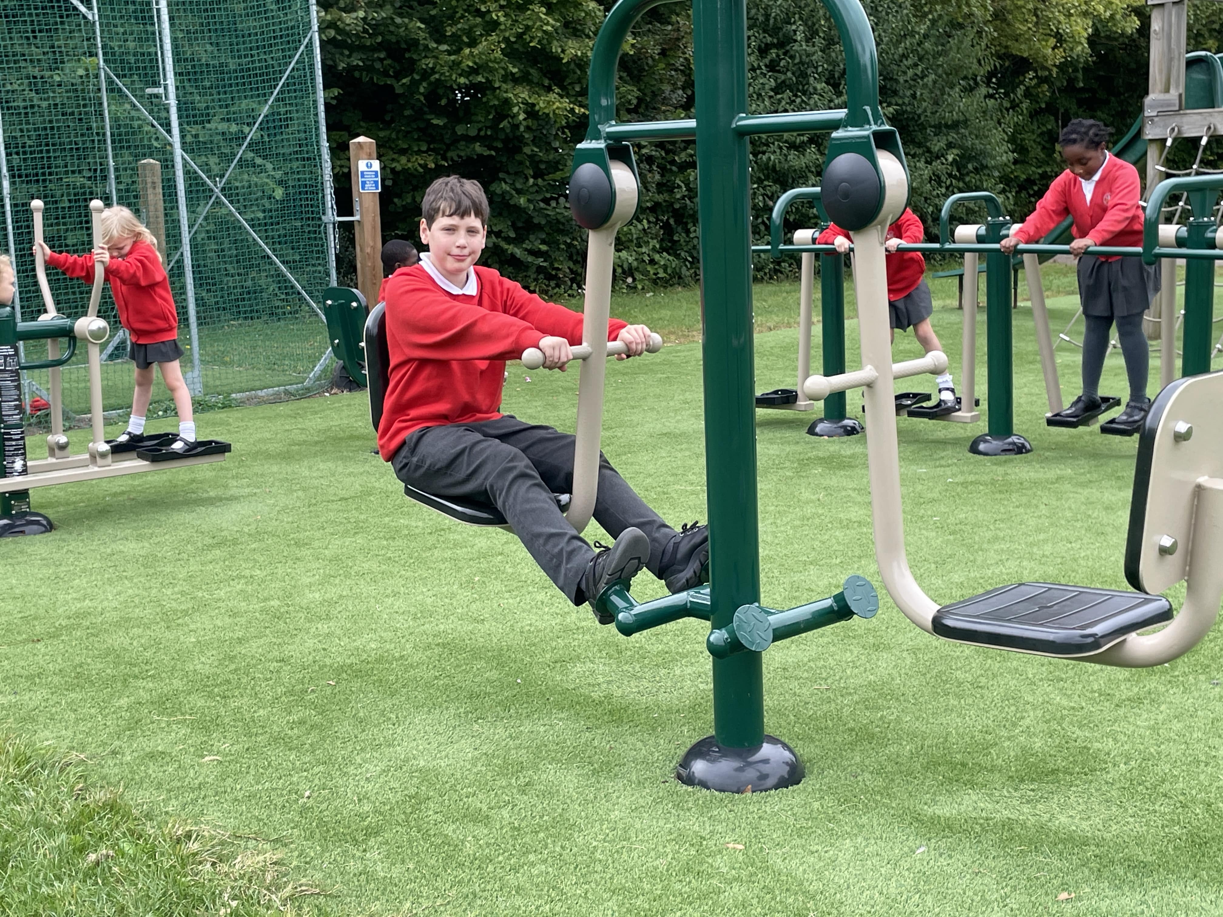 A child is using a piece of outdoor gym equipment as other children try different pieces of outdoor gym equipment behind him.