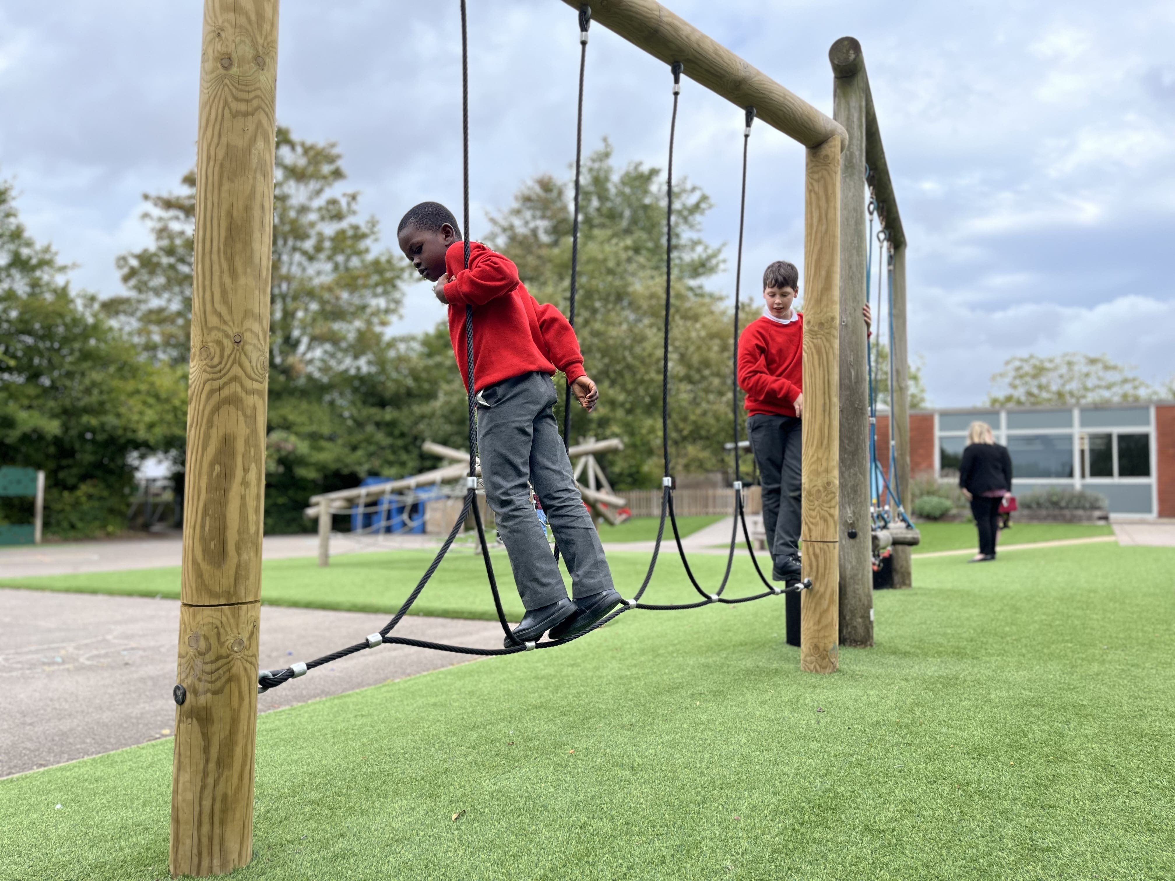 Children are playing on parts of a trim trail which has been installed on artificial grass