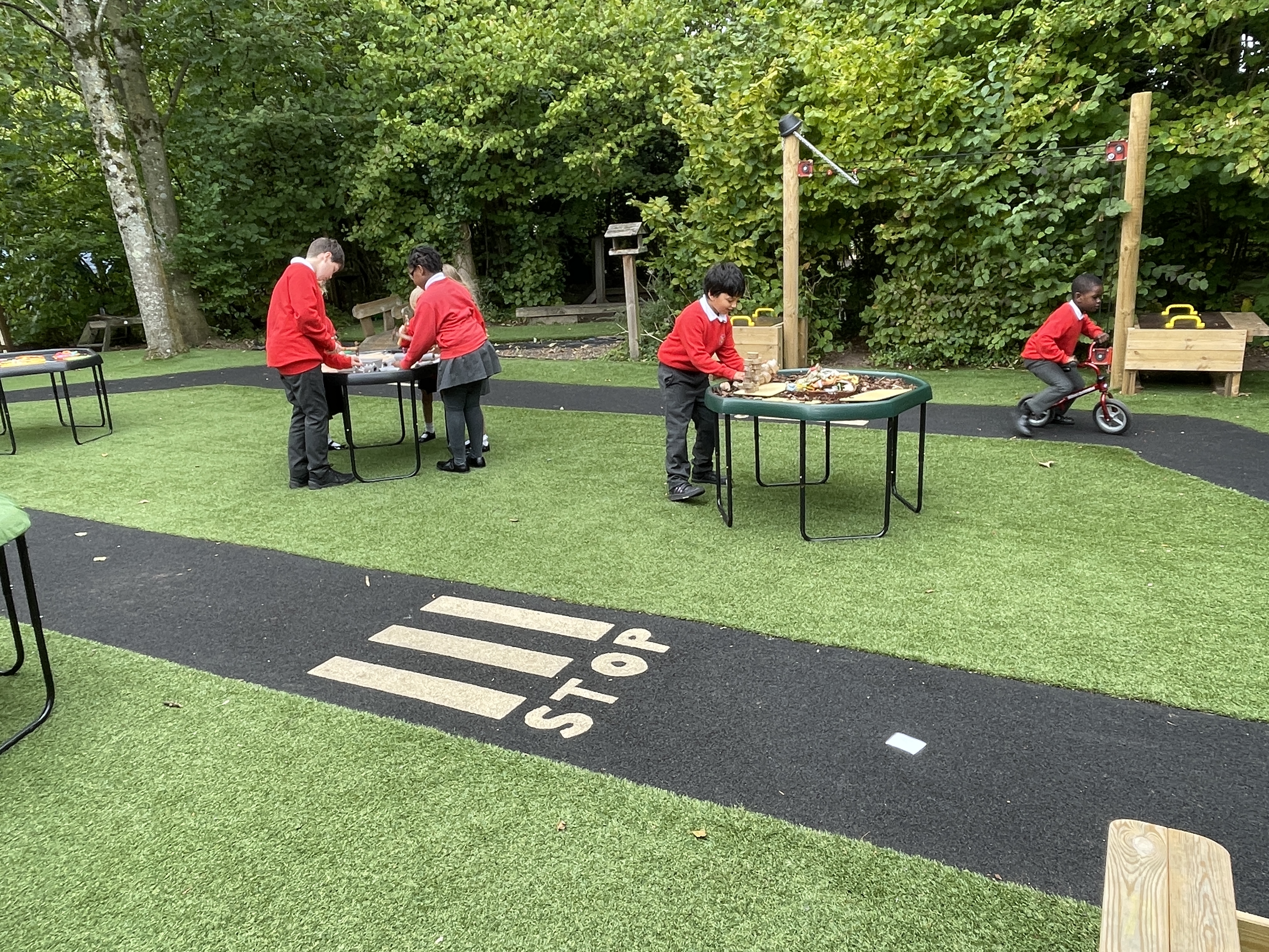 A group of children are playing on an artificial grass surface and are interacting with other pieces of play equipment.