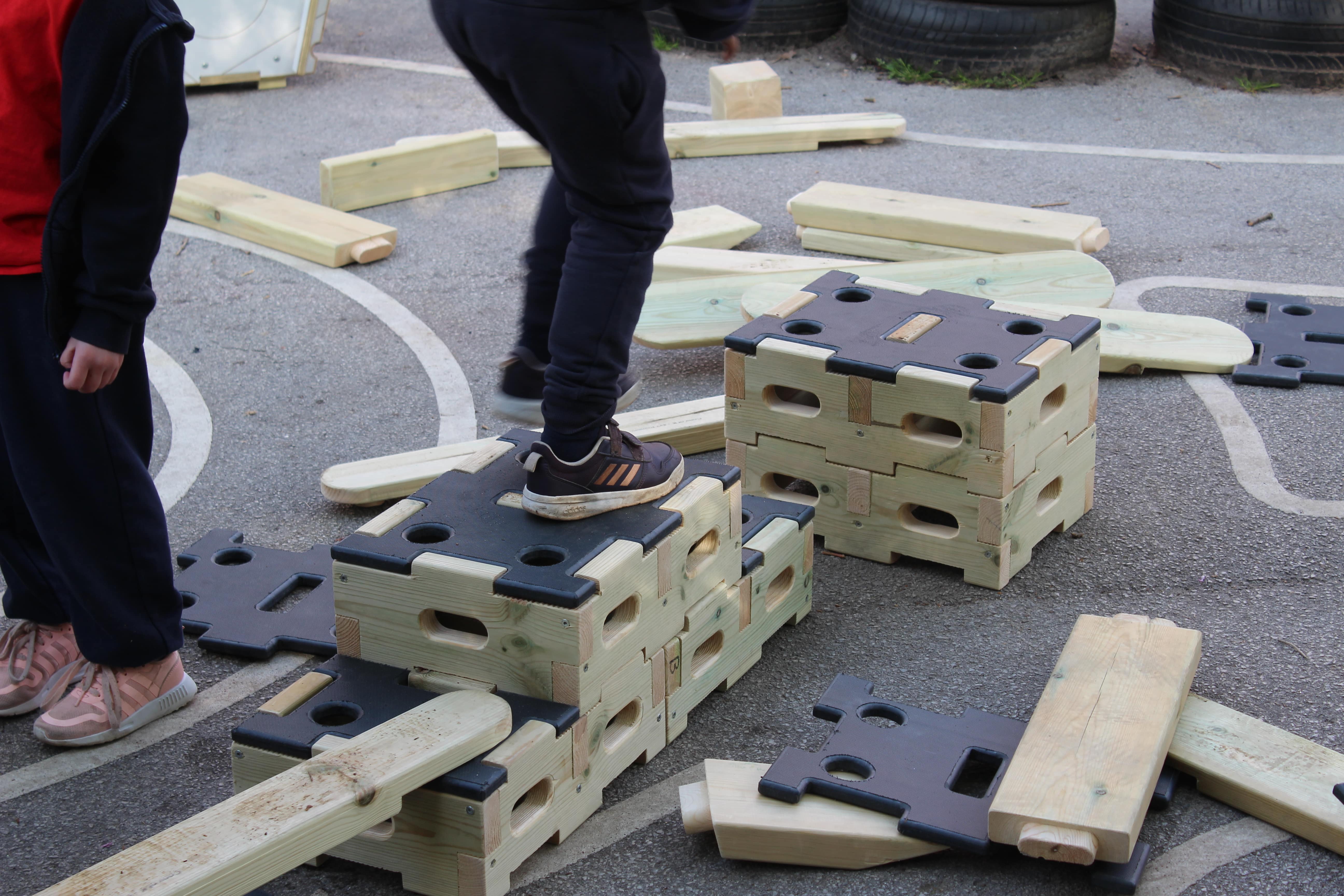 A close up of a 2 children stood on top of wooden blocks from the Play Builder Sets.