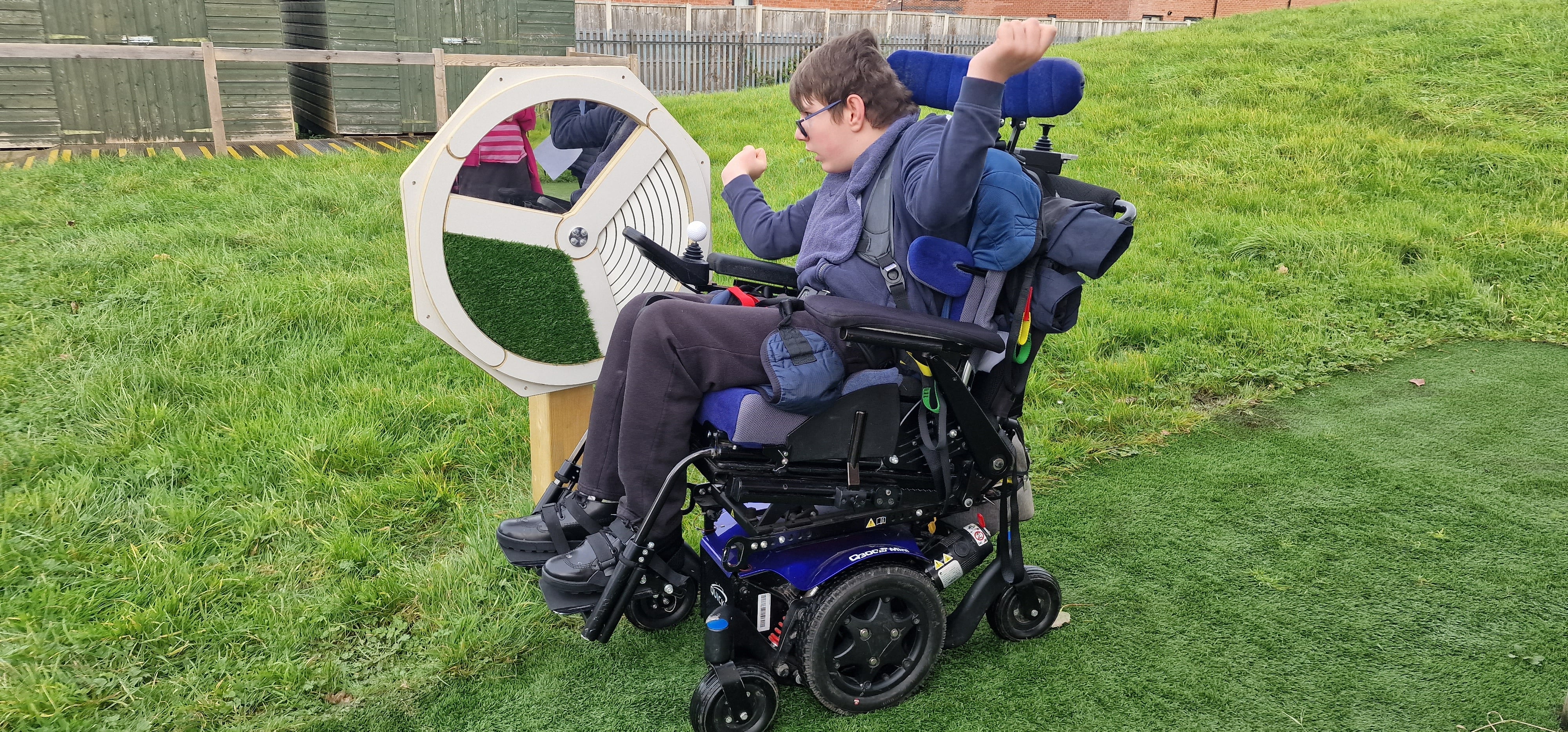 A child in a wheelchair is playing with a sensory spinner and smiling.