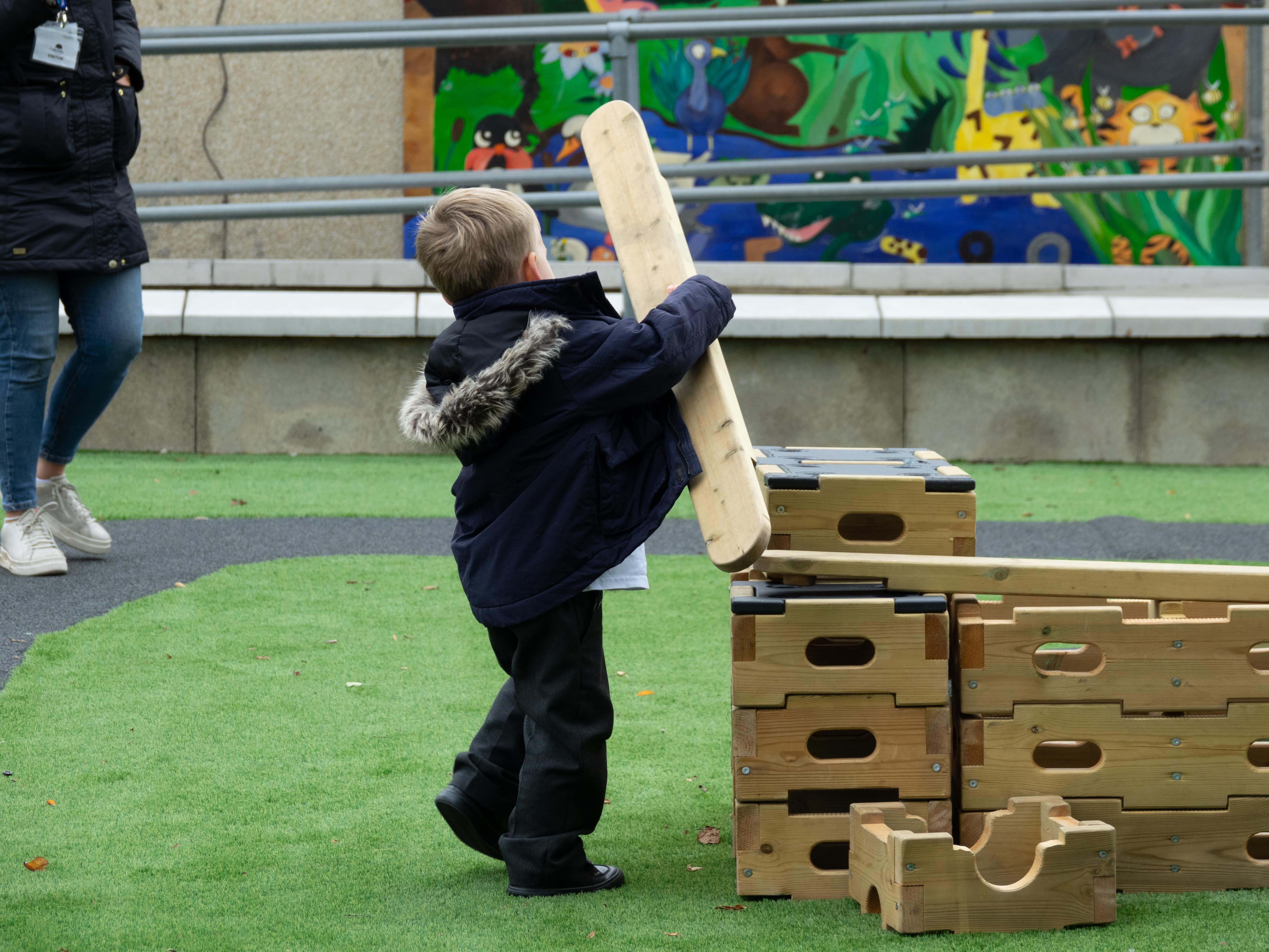 A little boy is holding a wooden plank and is moving it from a pile.