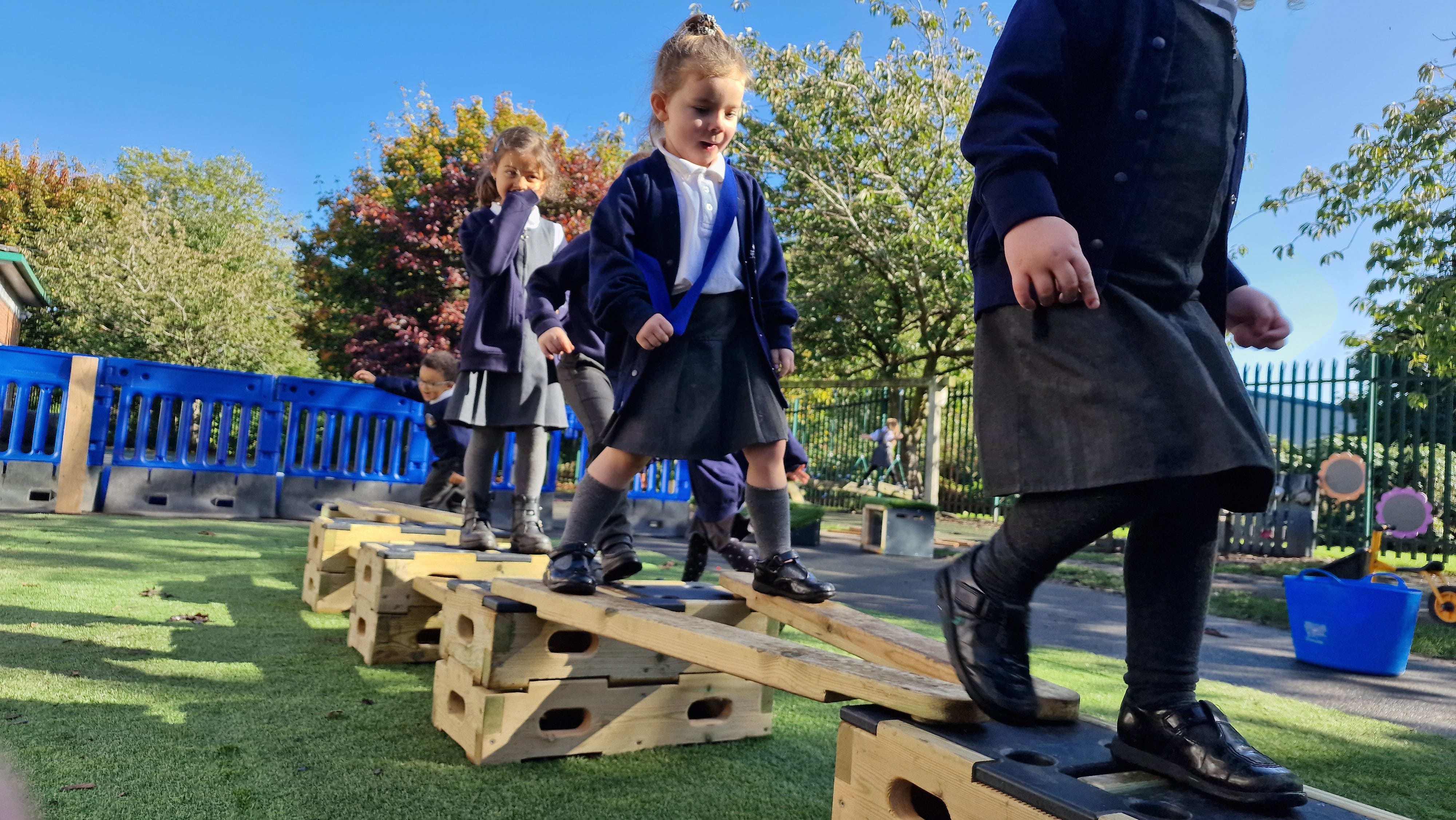 Children walking across a wooden plank from the Play Builder set, improving their vestibular and proprioceptive skills.