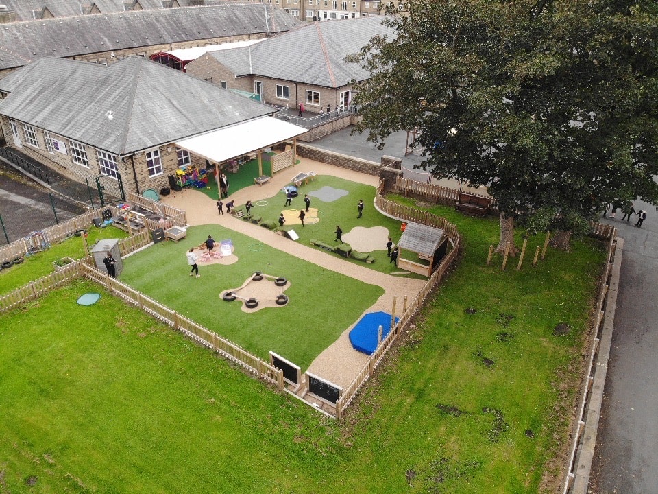 An artificial grass playground that features a variety of playground equipment on it, surrounding by wooden fencing.