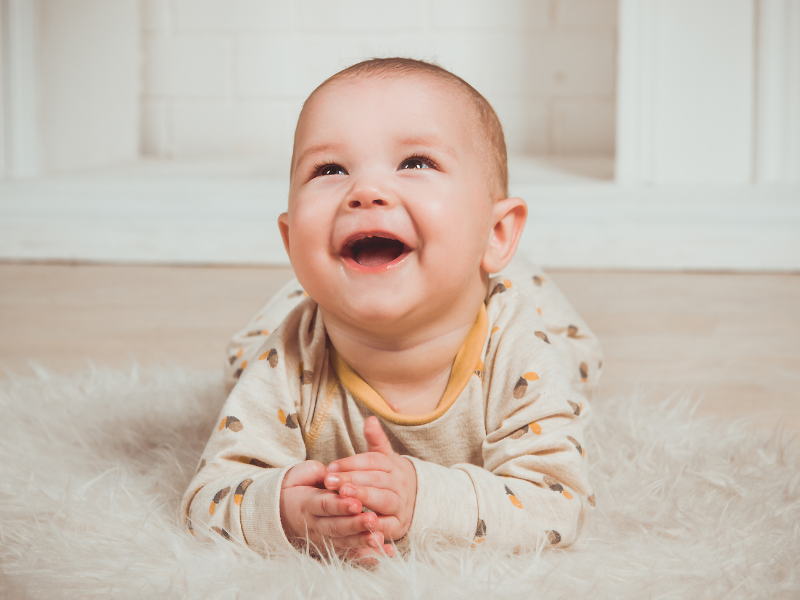 A baby looking above the camera and laughing. The baby is lay on it's stomach.