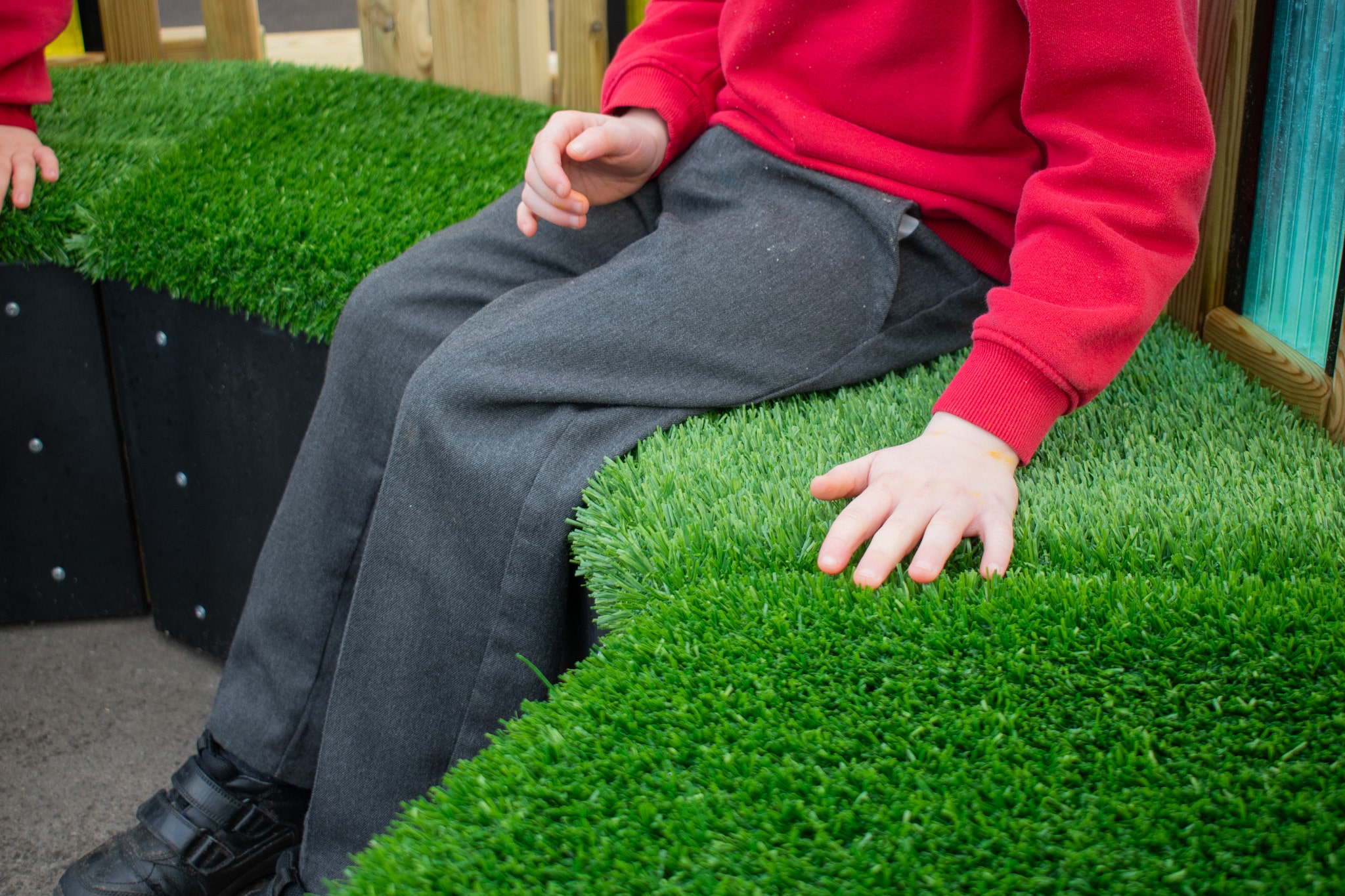 A little boy is rubbing his hand against the artificial grass top on the Sensory Seating Circle