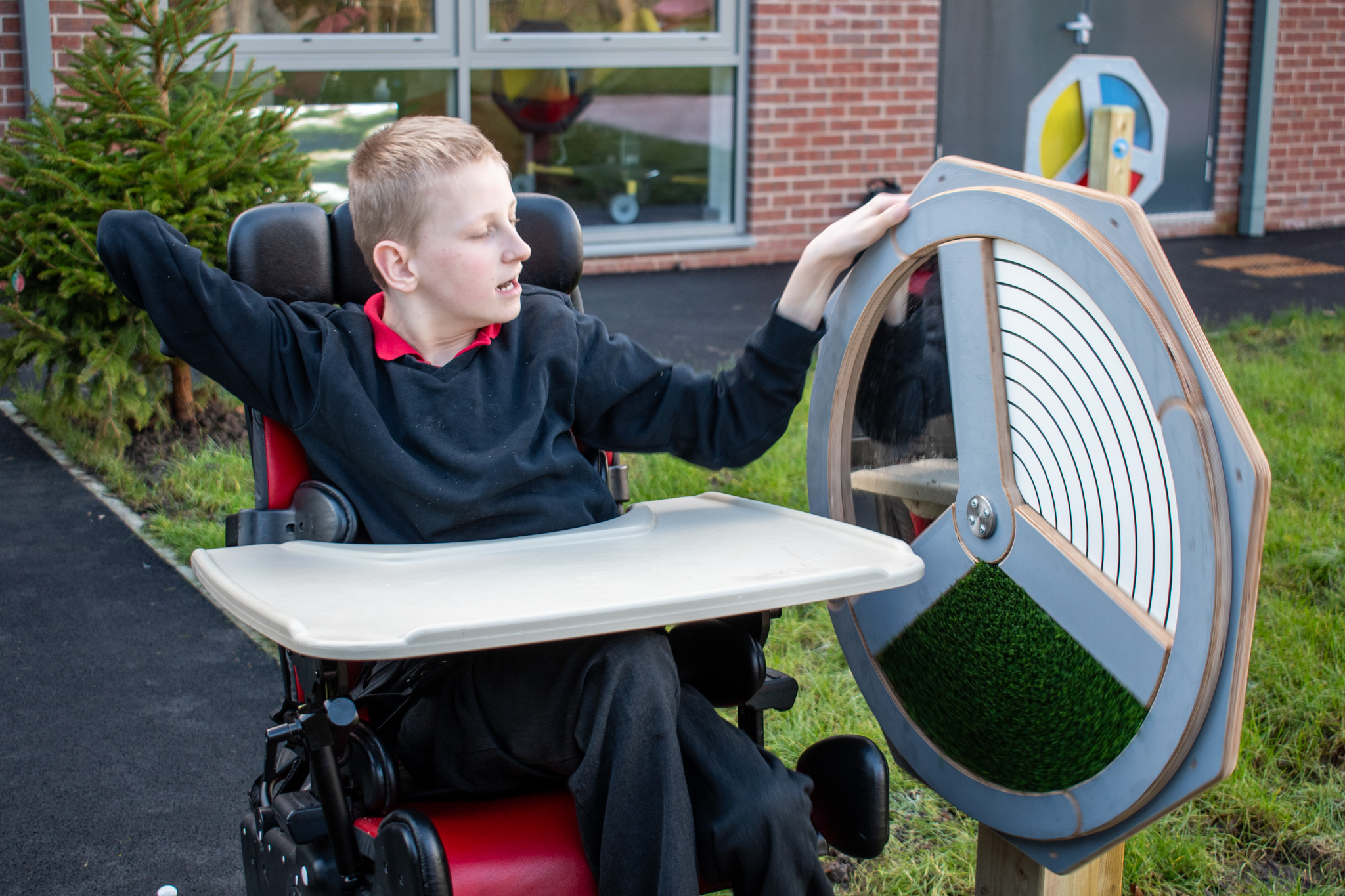 A boy in a wheelchair has his hand on the Touch Sensory Spinner and is about to spin in. He looks intrigued with the equipment.