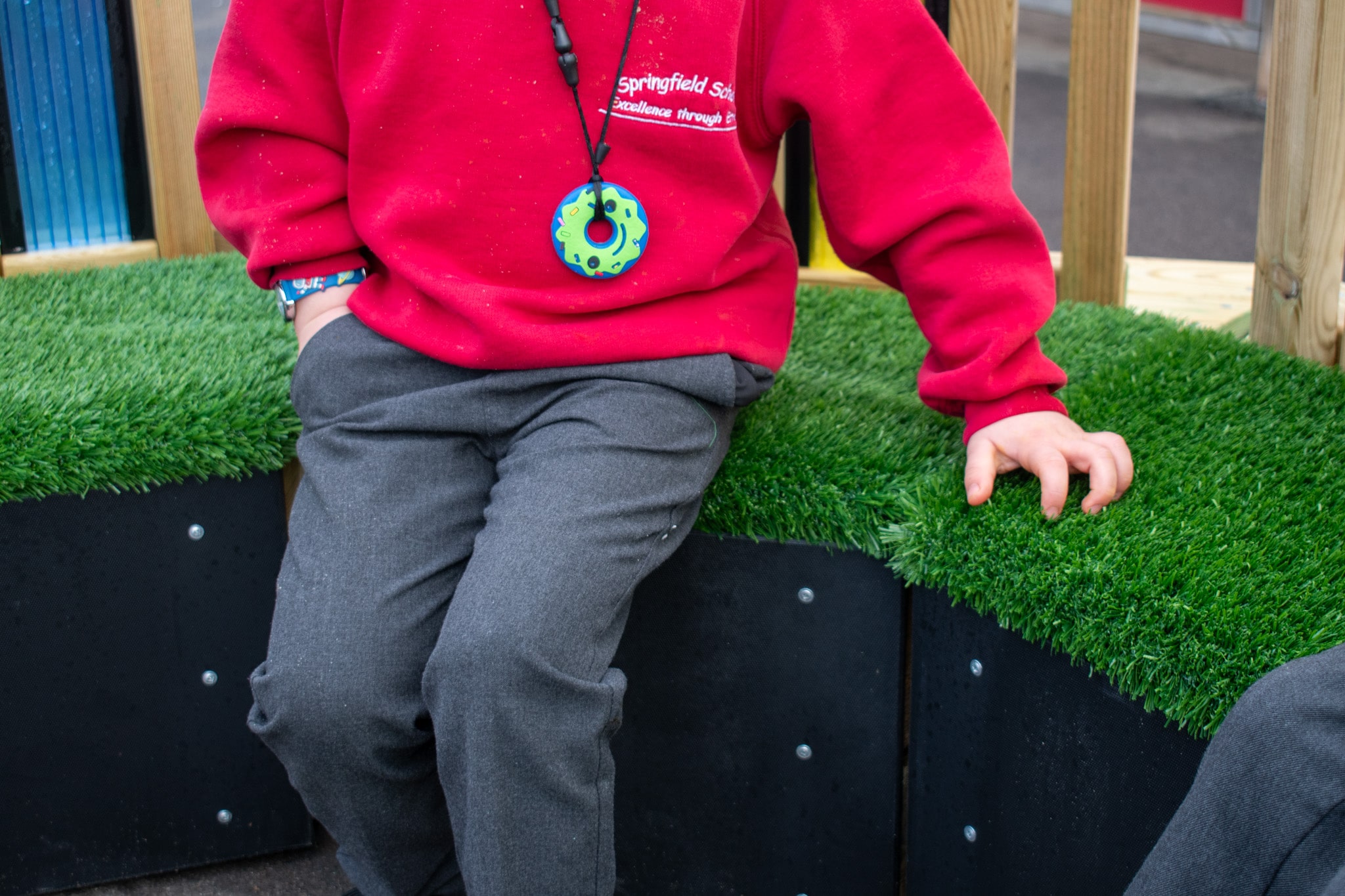 A child is rubbing their hand against the artificial grass placed on top of the Sensory Seating Circle seats.