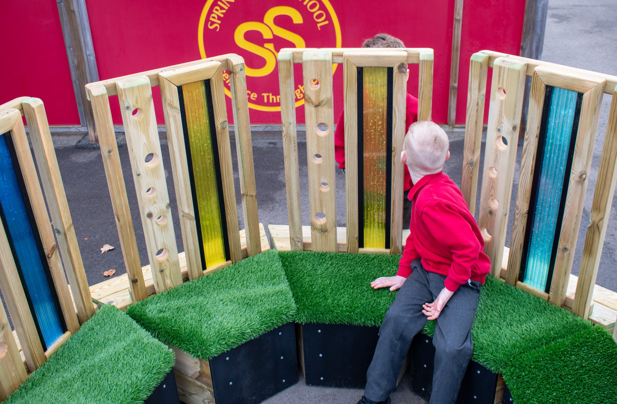 Two boys are stood on opposite sides of the coloured translucent plastic featured on the Sensory Seating Circle. 