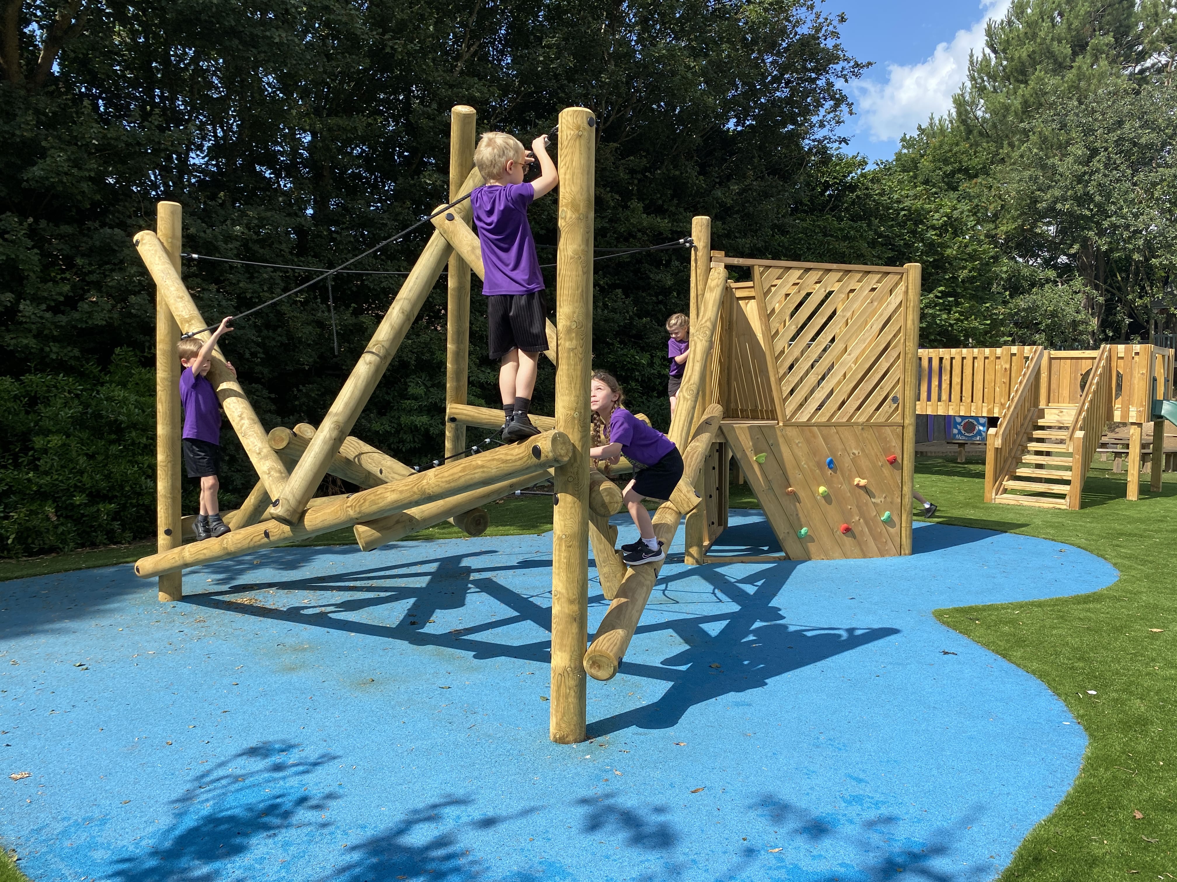 A huge climbing frame with an attached climbing wall and platform has been installed on top of blue artificial grass.