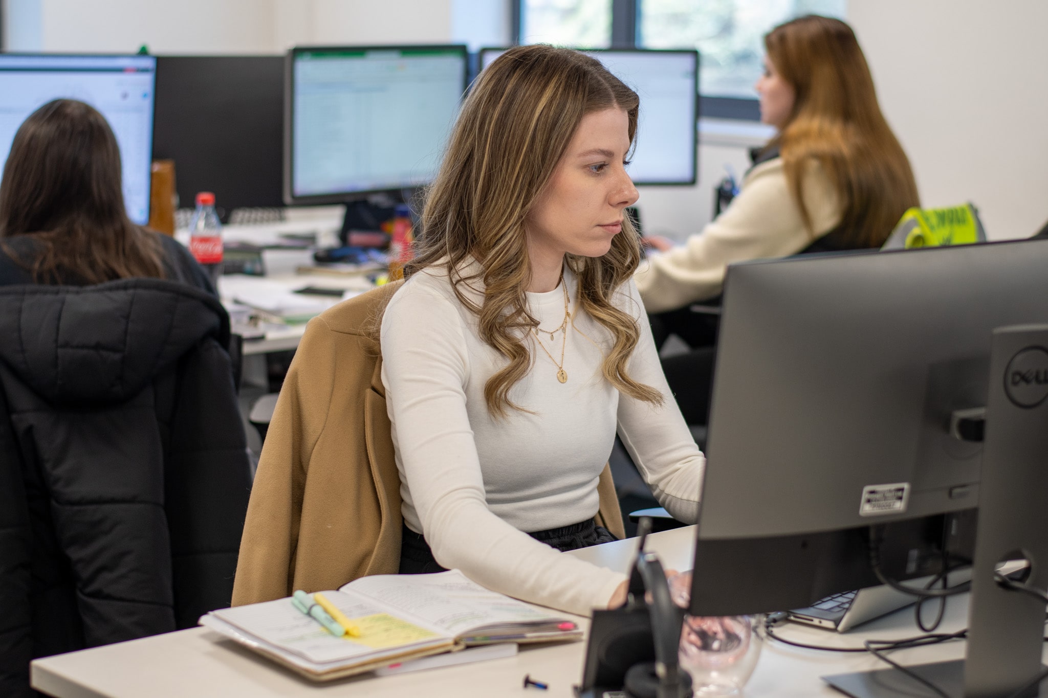 Tara Shelton-Lefley is working at her computer and two other employees can be seen behind her working hard too.