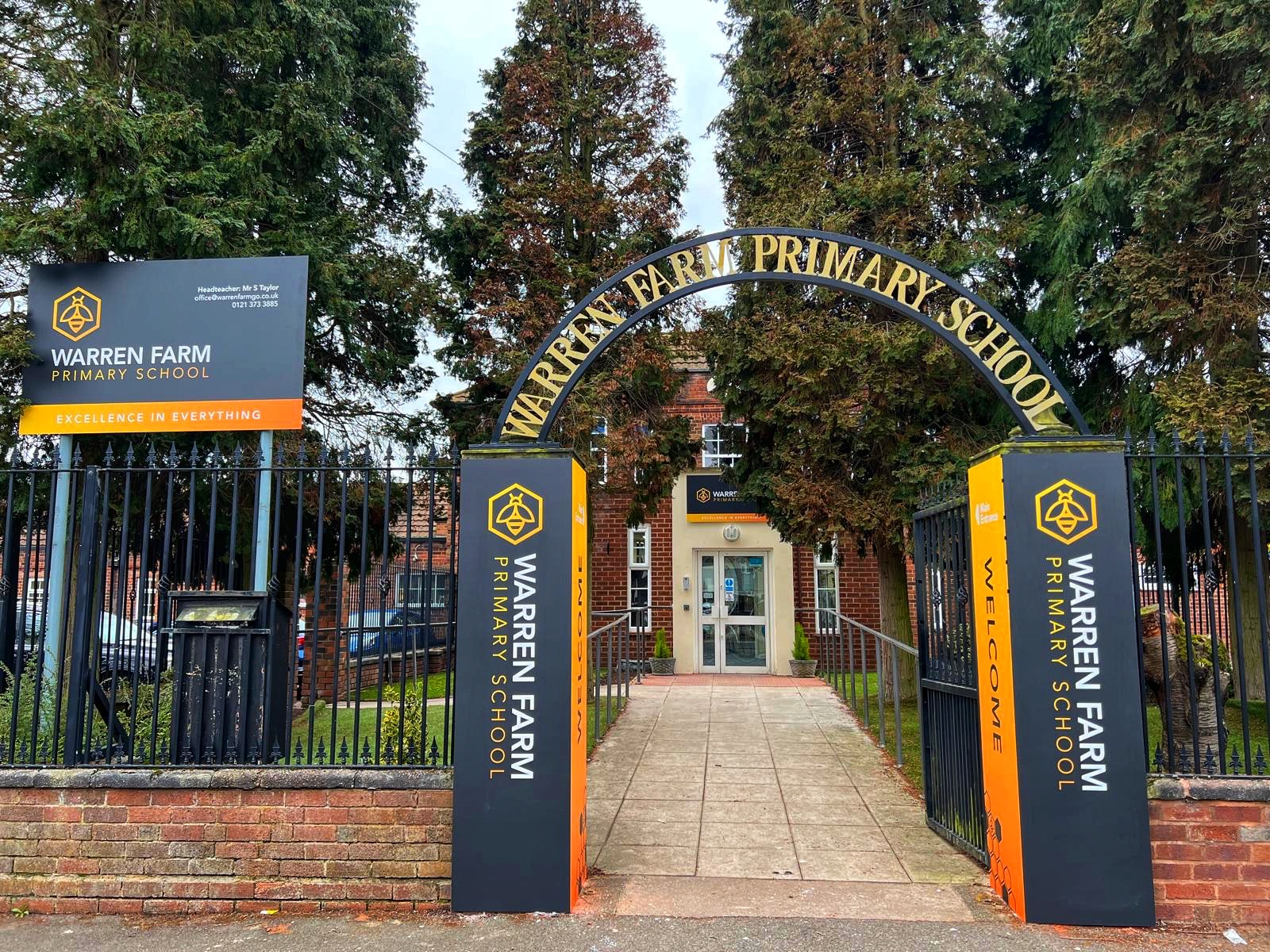 The outside gate of Warren Farm Primary School, with the logo placed above the gate and the bee next to it.