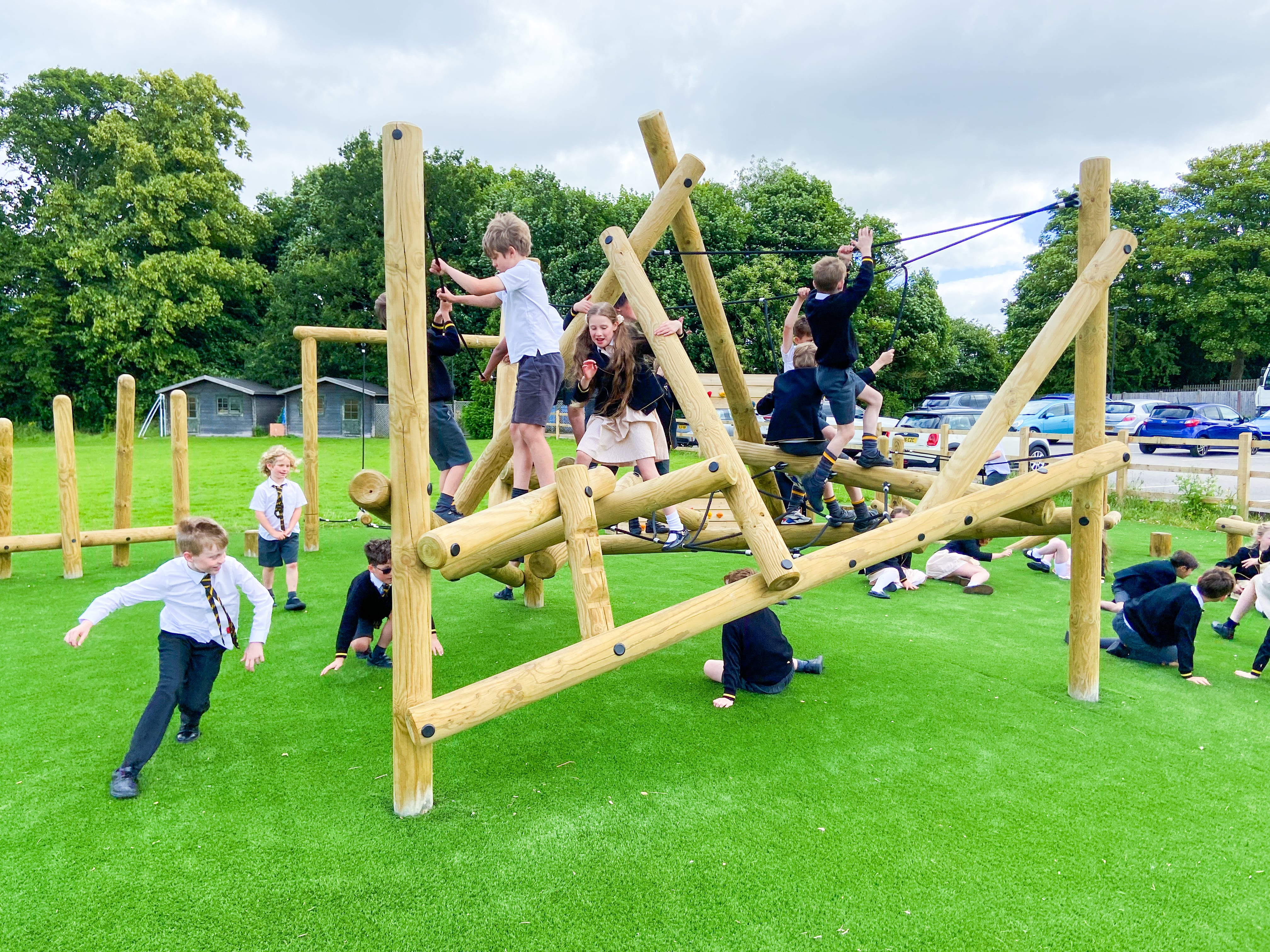 A large group of children are exploring the Bowfell Climber, with some children climbing on it and others going underneath.