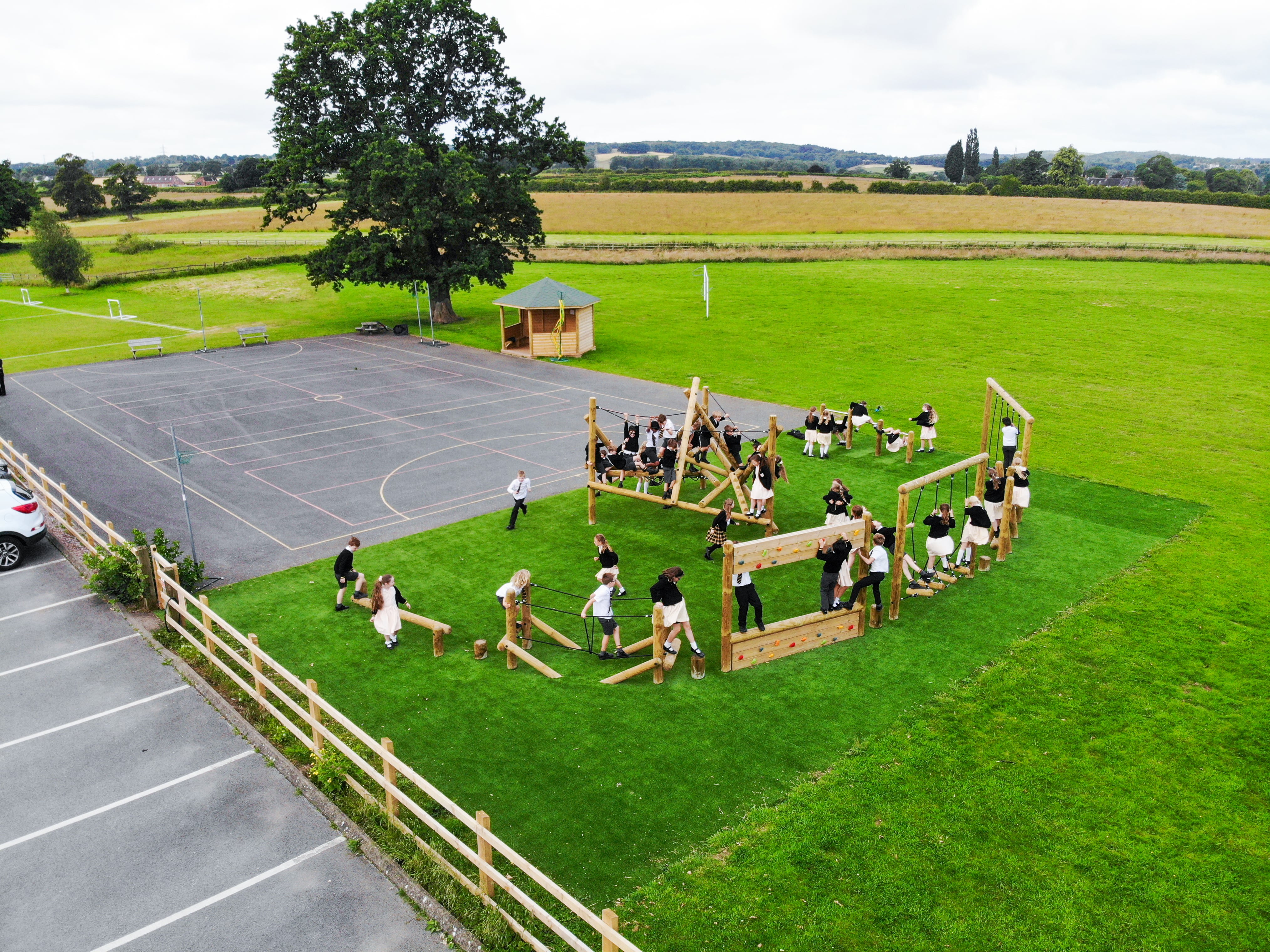 The entire trim trail with the Bowfell Climber in the middle of the artificial grass surfacing. A bespoke gazebo can be seen beside the tarmac playground.