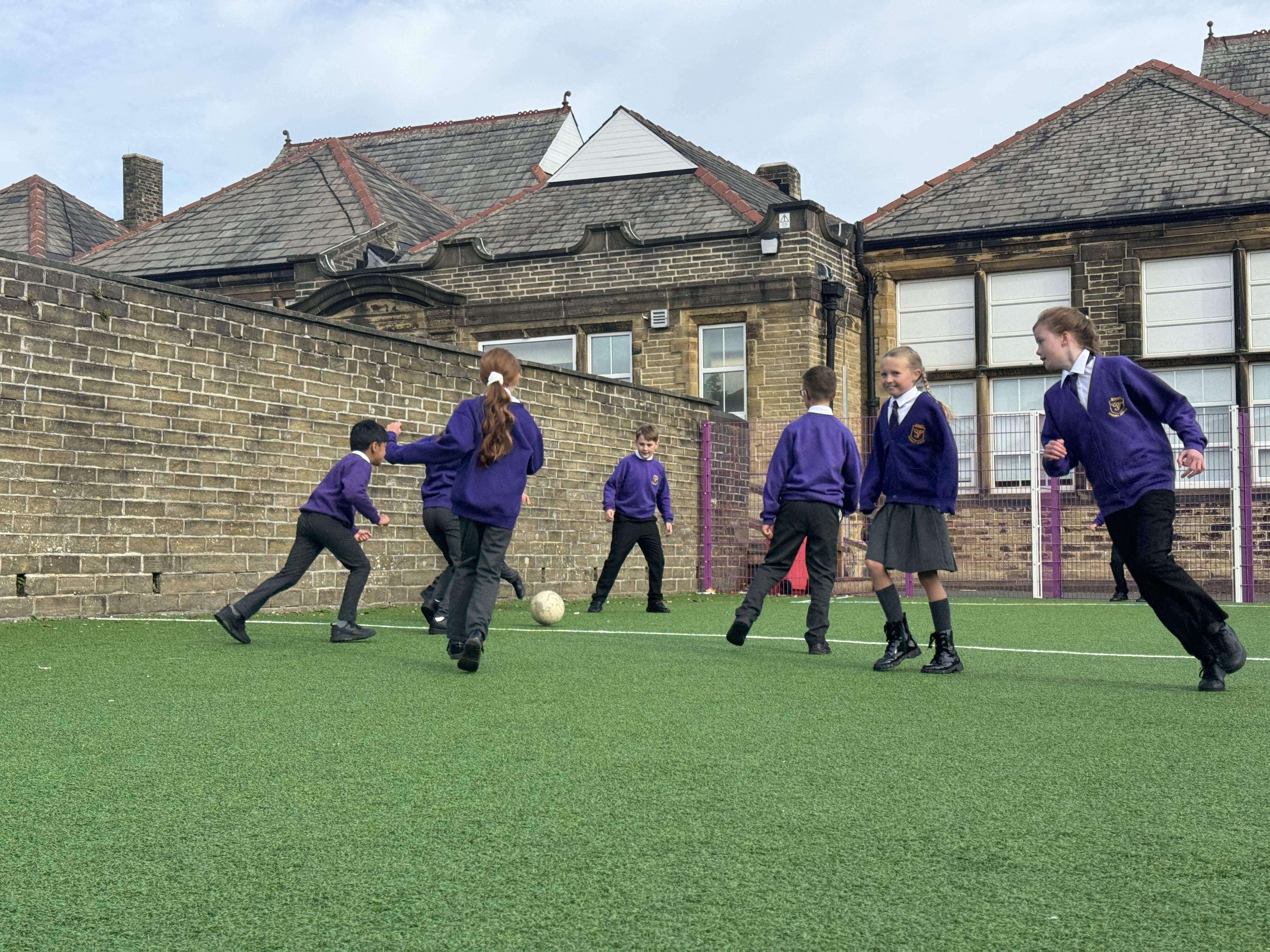 A large group of children are playing football on artificial grass.