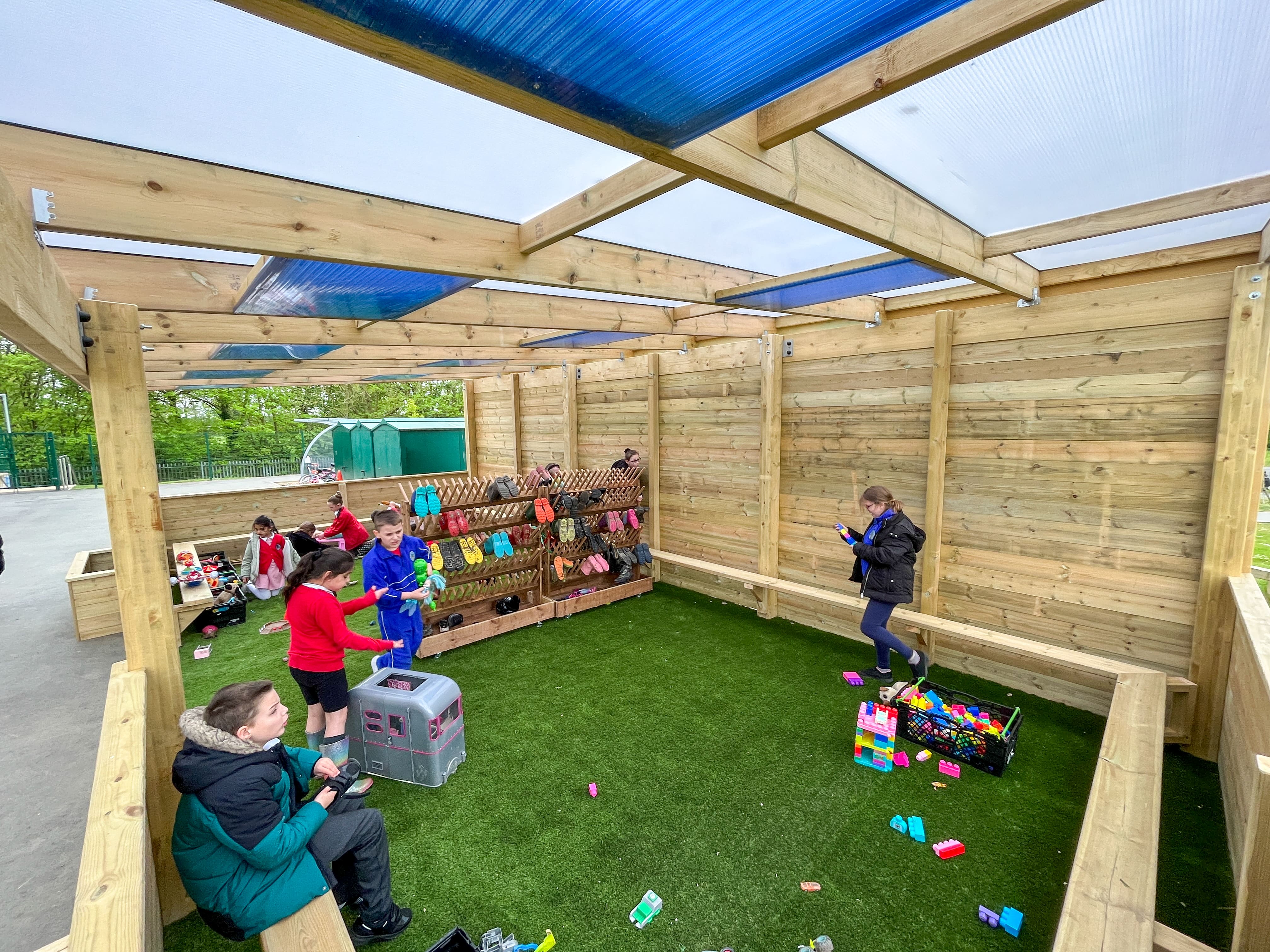 Artificial grass surfacing that has been placed underneath a freestanding timber canopy. Children are on top of the surface.