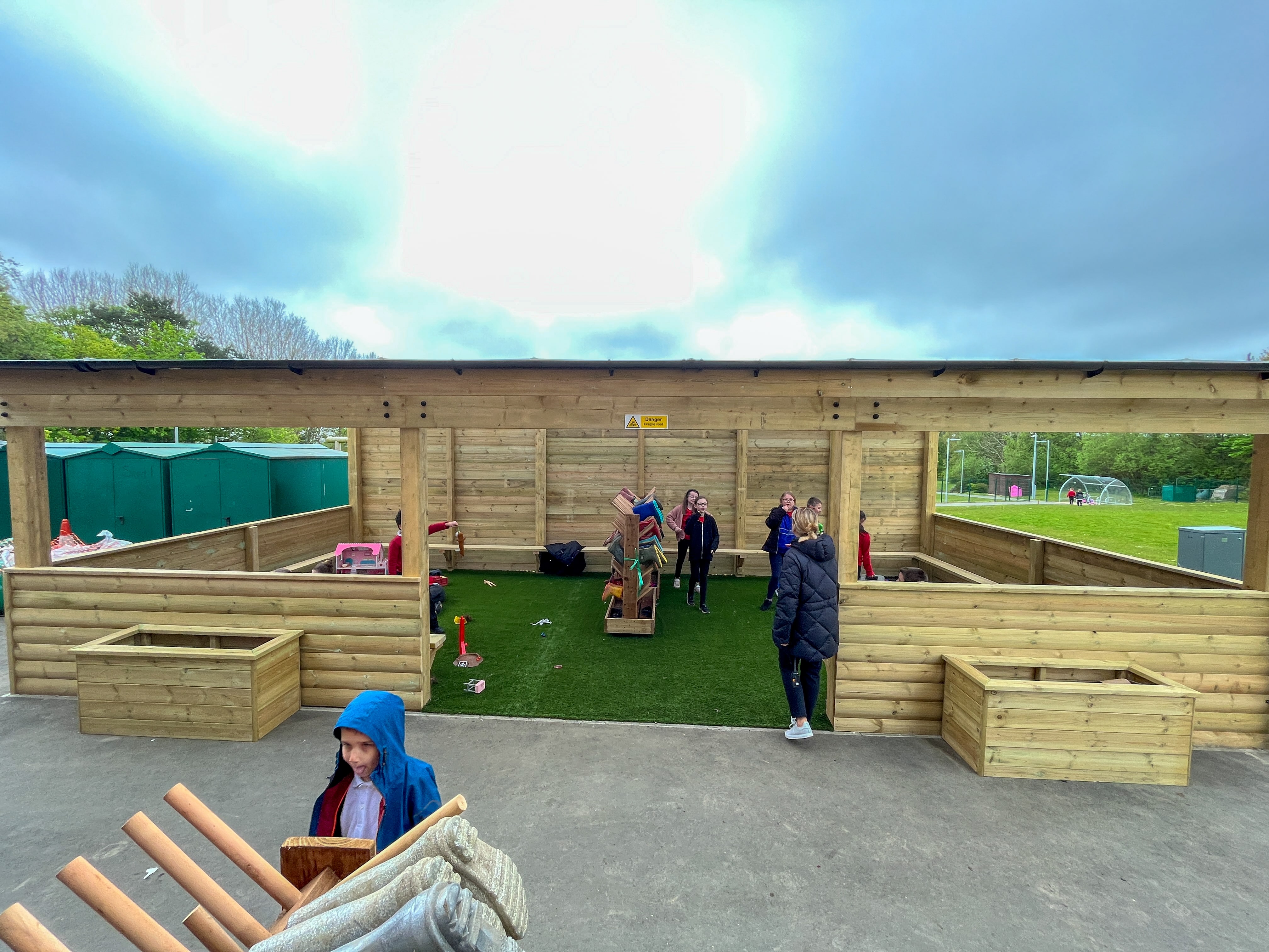 A timber freestanding canopy that has a group of children inside it and engaging with different pieces of equipment.