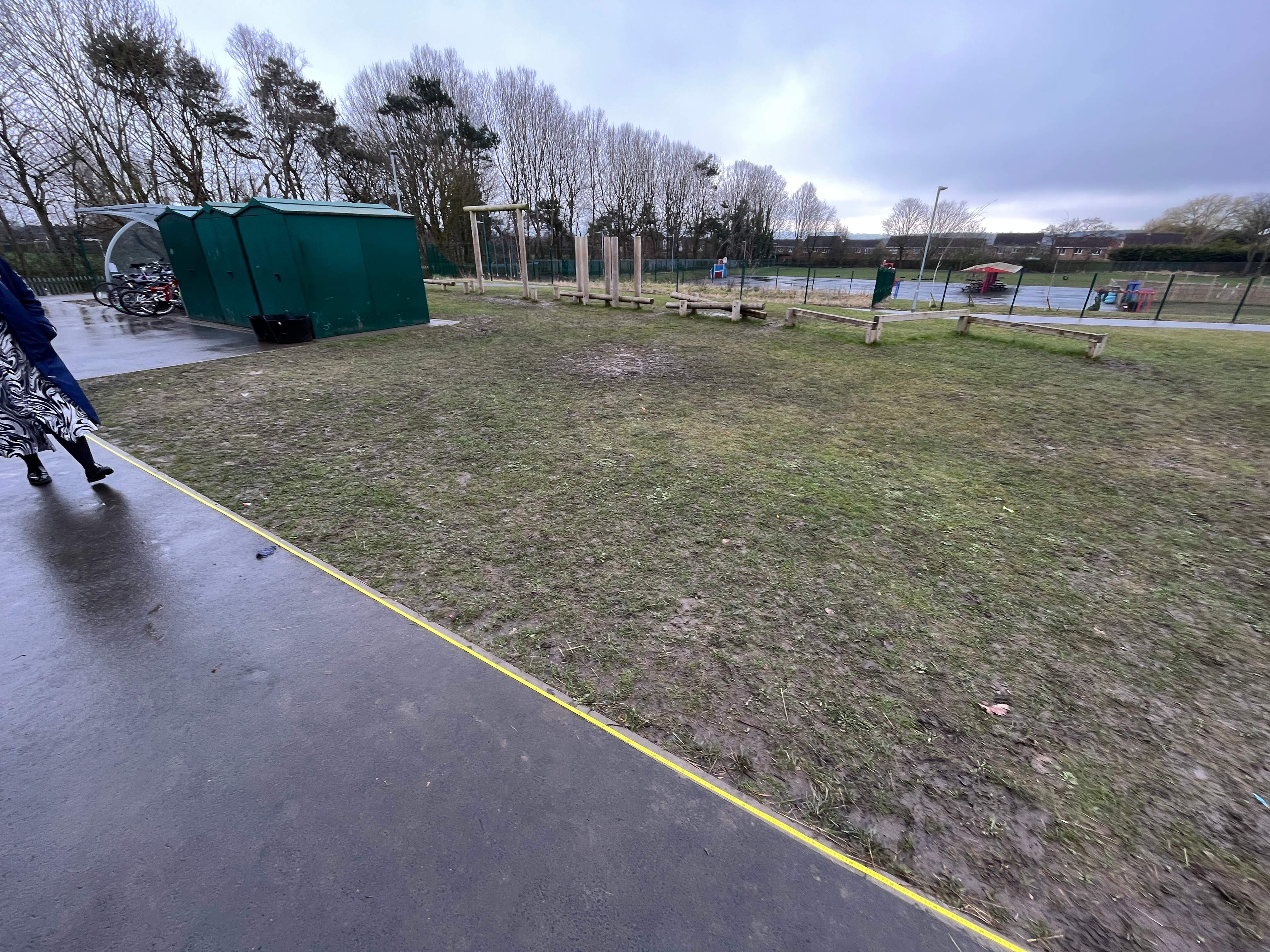 A natural grass area that has been marked out with yellow tape, beside a tarmac playground.