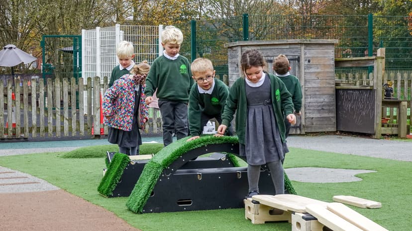 A large group of children are climbing over the rockies and are making their way across the play builder planks.