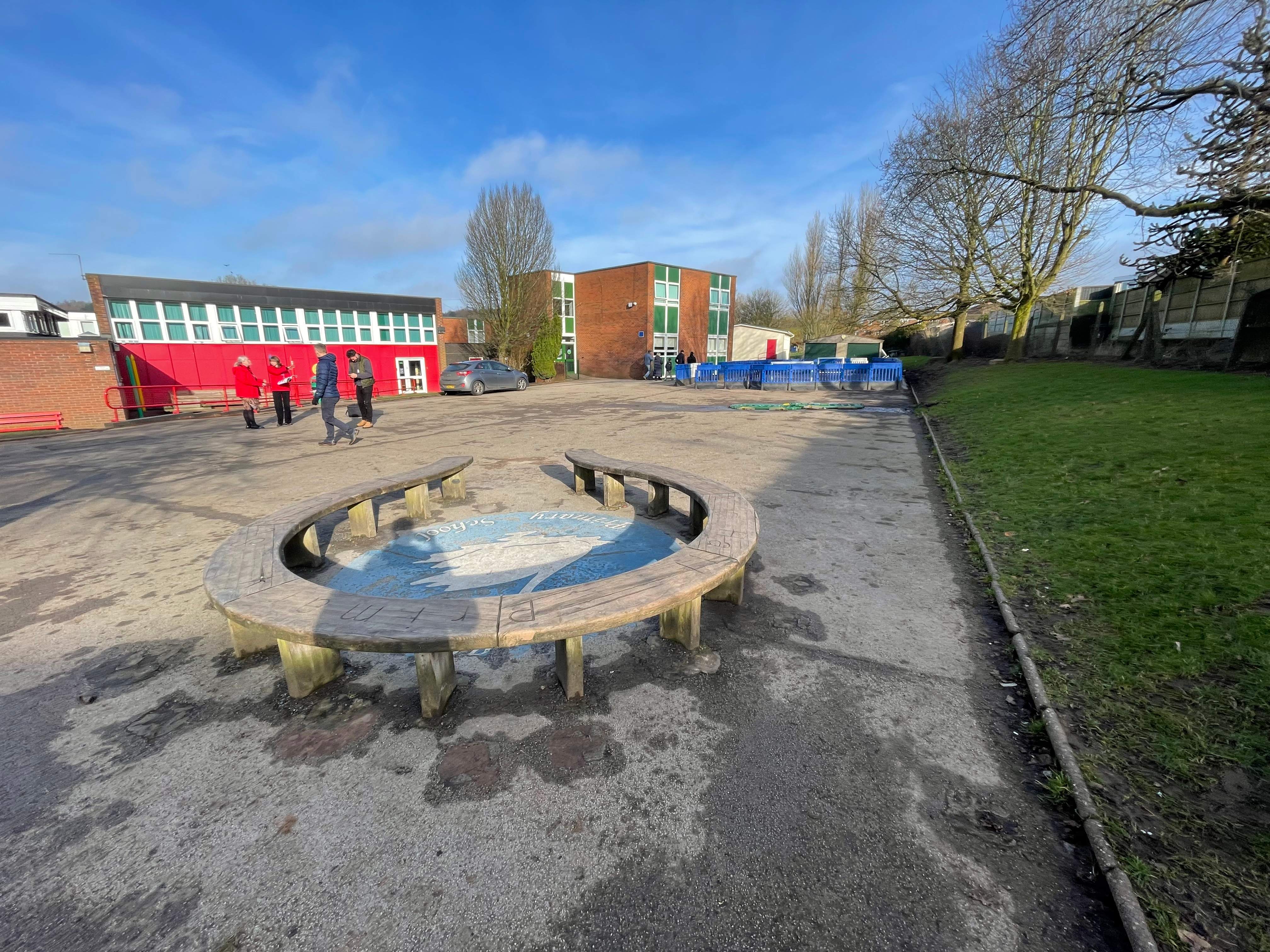 A tarmac playground that is behind a school, with a concrete seating circle.