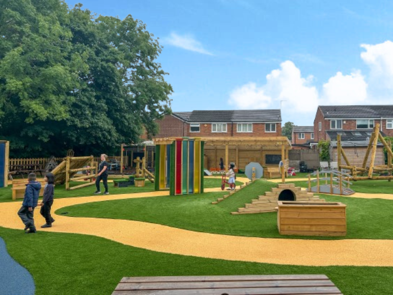A group of children are exploring the new play area, with artificial grass and wetpour surfacing.