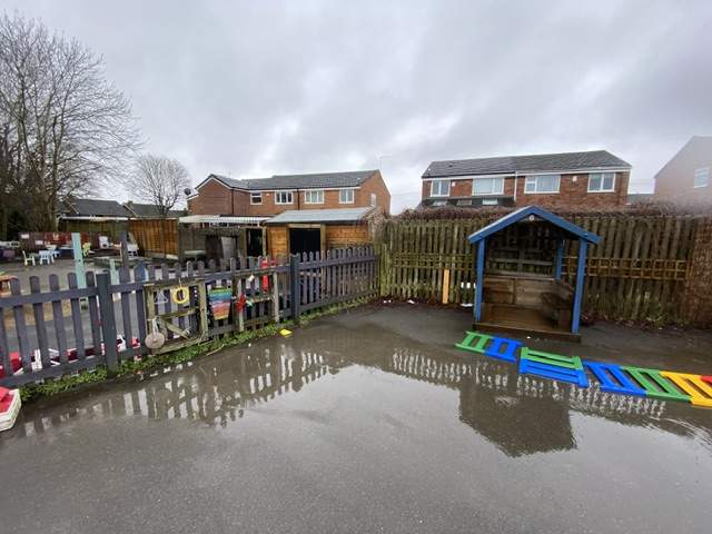 A flooded old playground, with a wooden fence separating the area into two.