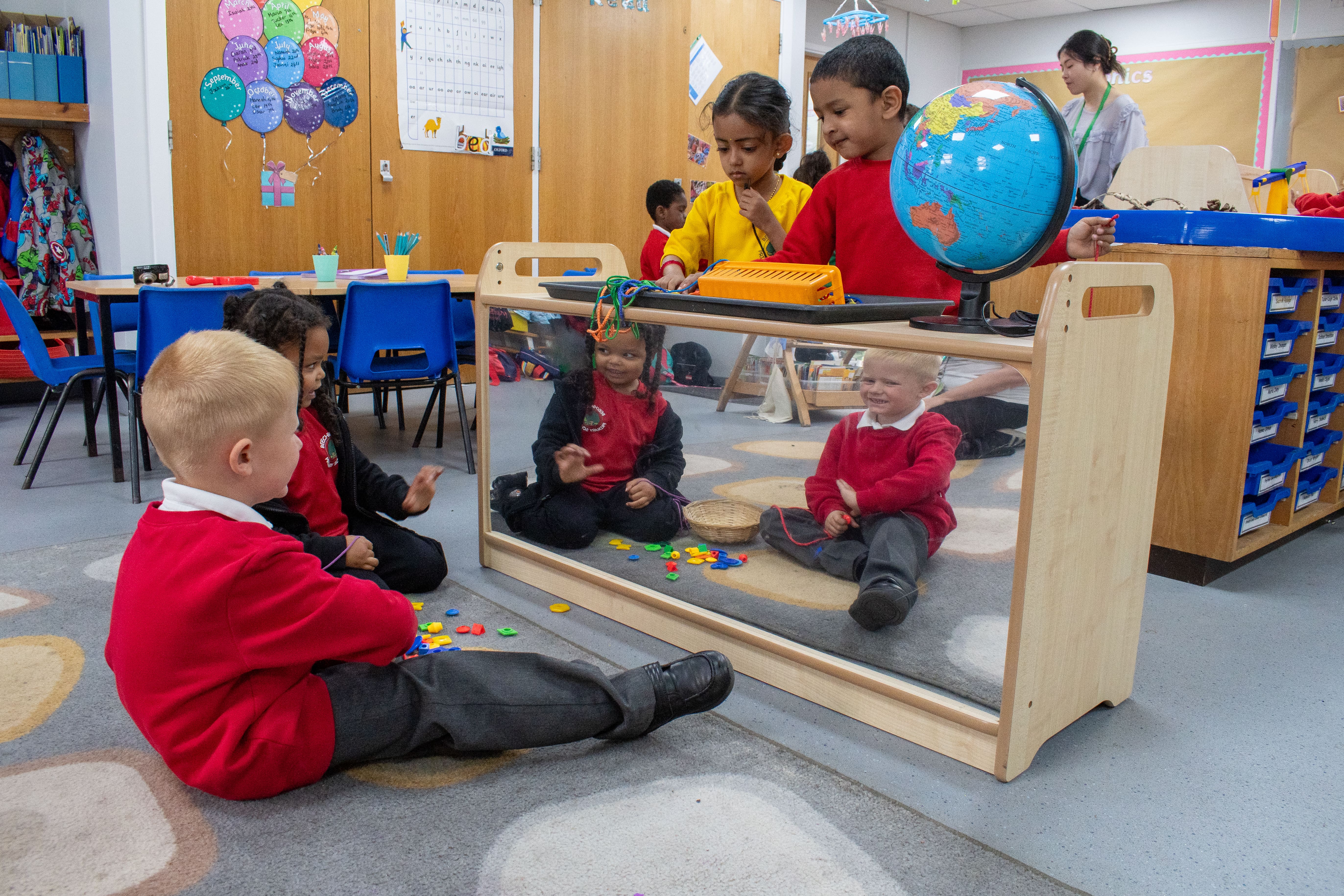 Two children are sat on the floor and looking at their reflections in the mirror as two other children are working on the surface.