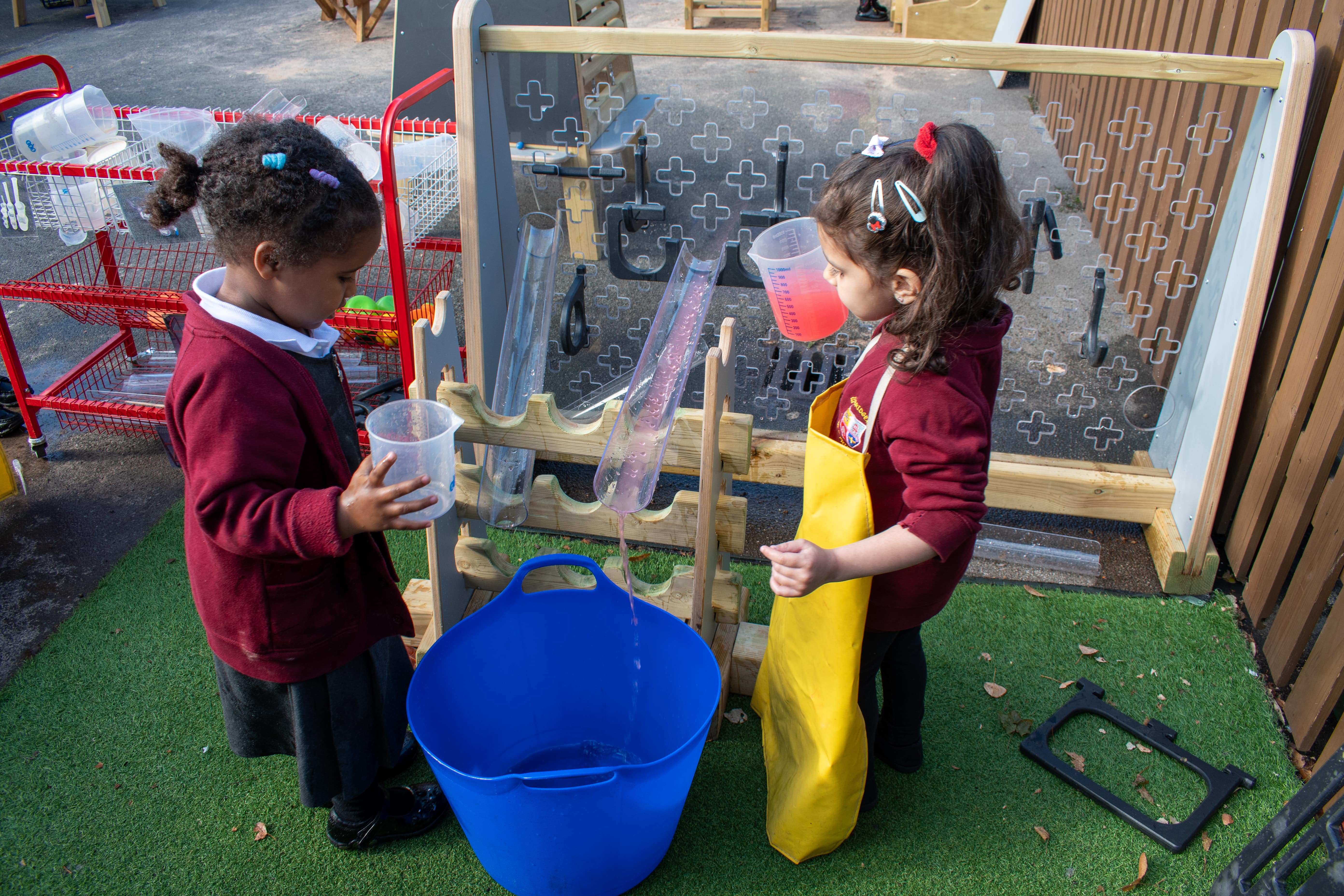 Two children are playing with a freestanding water wall and are watching water enter a bucket.