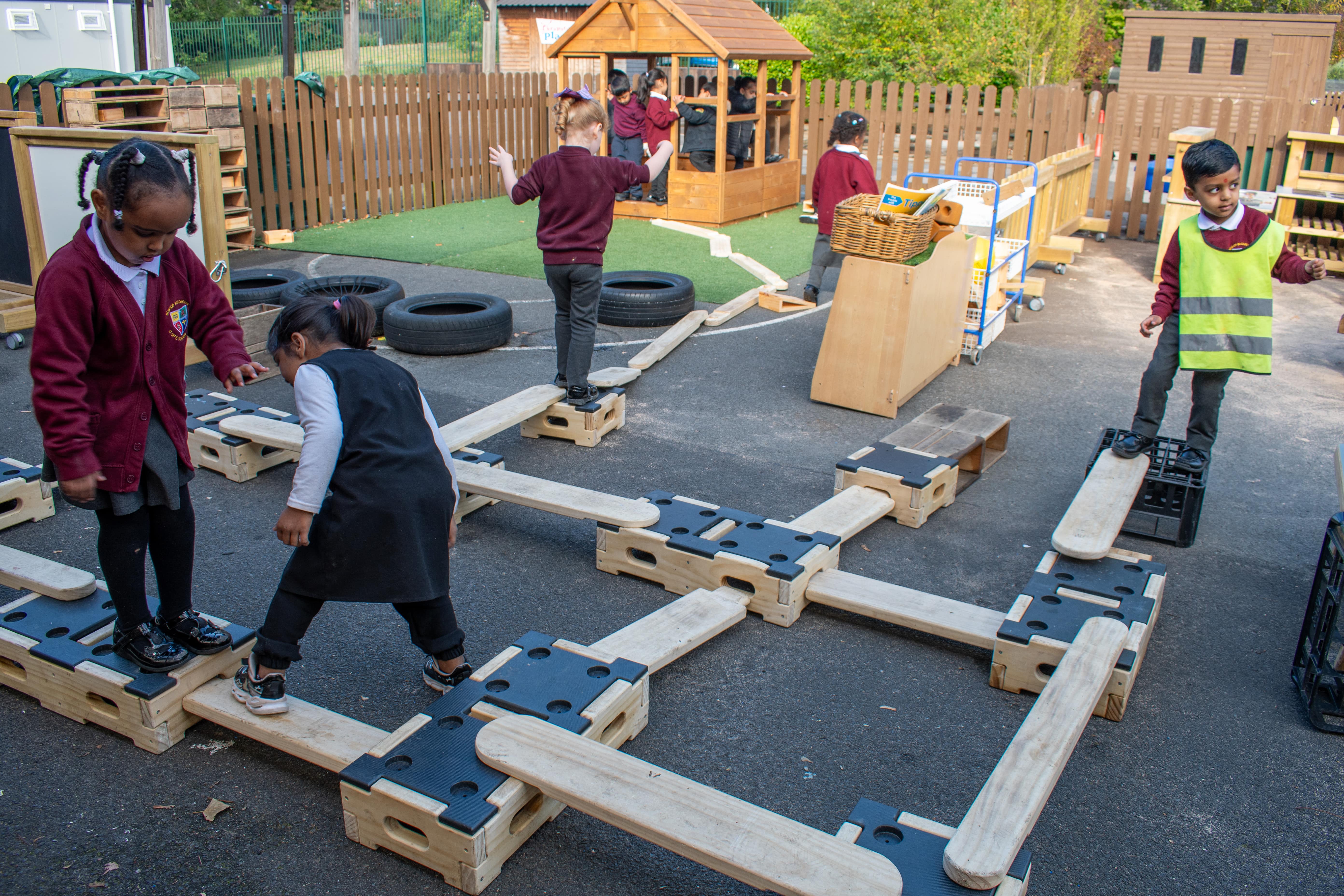 A large group of children are playing on a Play Builder set, crossing different wooden planks.