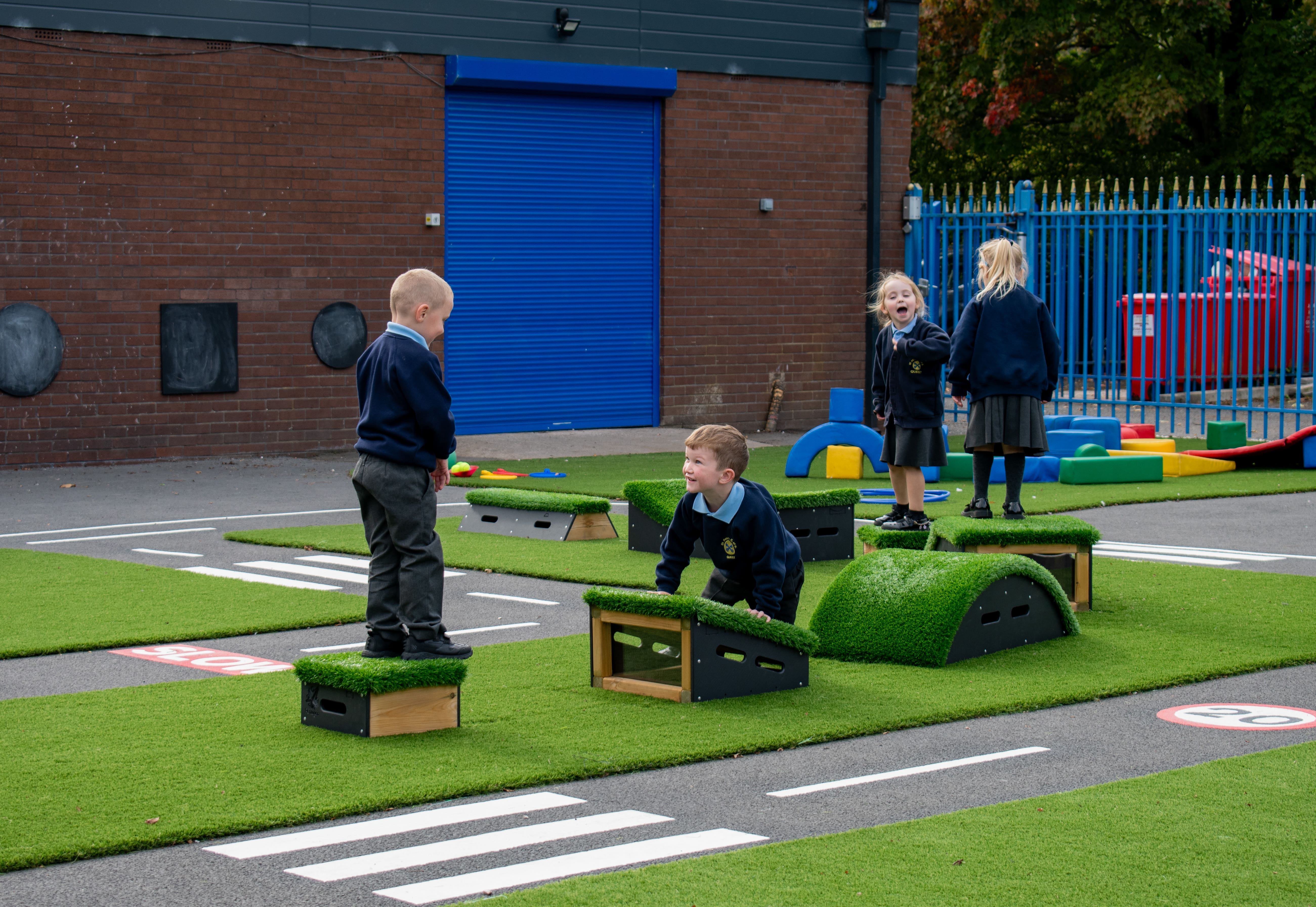A group of children are stood on the Get Set Go Blocks that are placed on artificial grass.