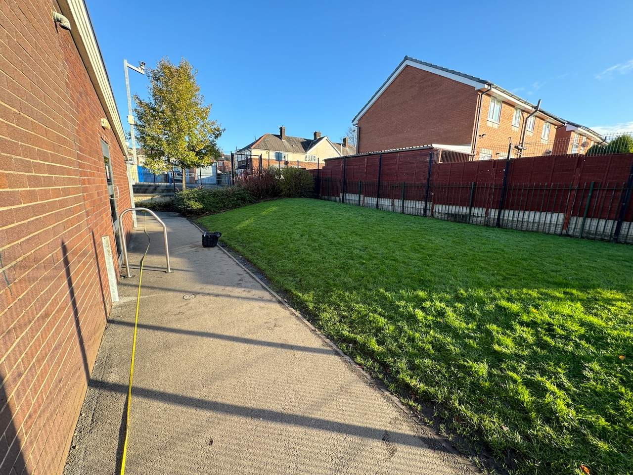 A small natural grass play area with a tarmac walkway at Hindley Green Primary.