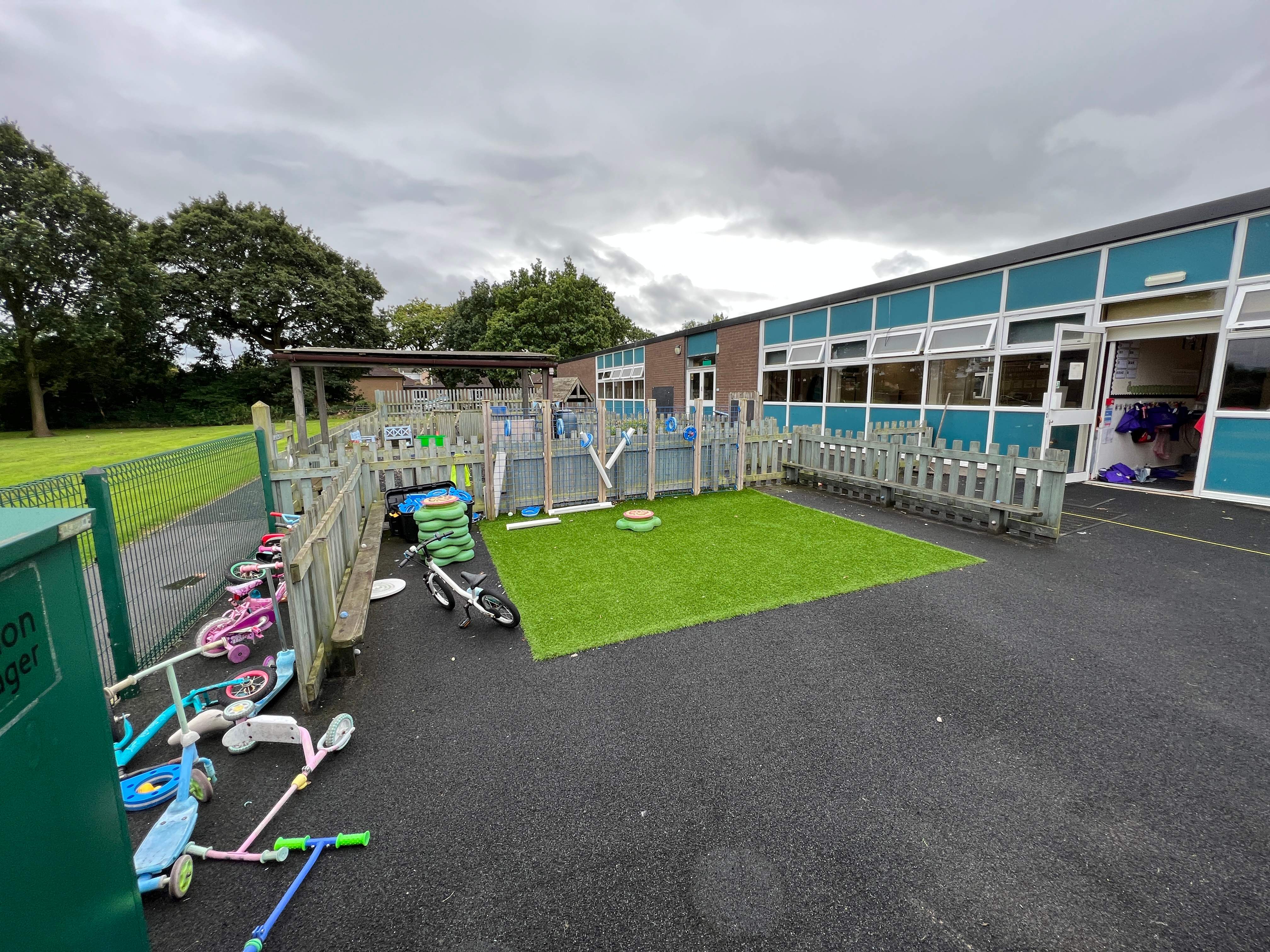 An old playground that has dull tarmac surfacing, with a small patch of artificial grass.