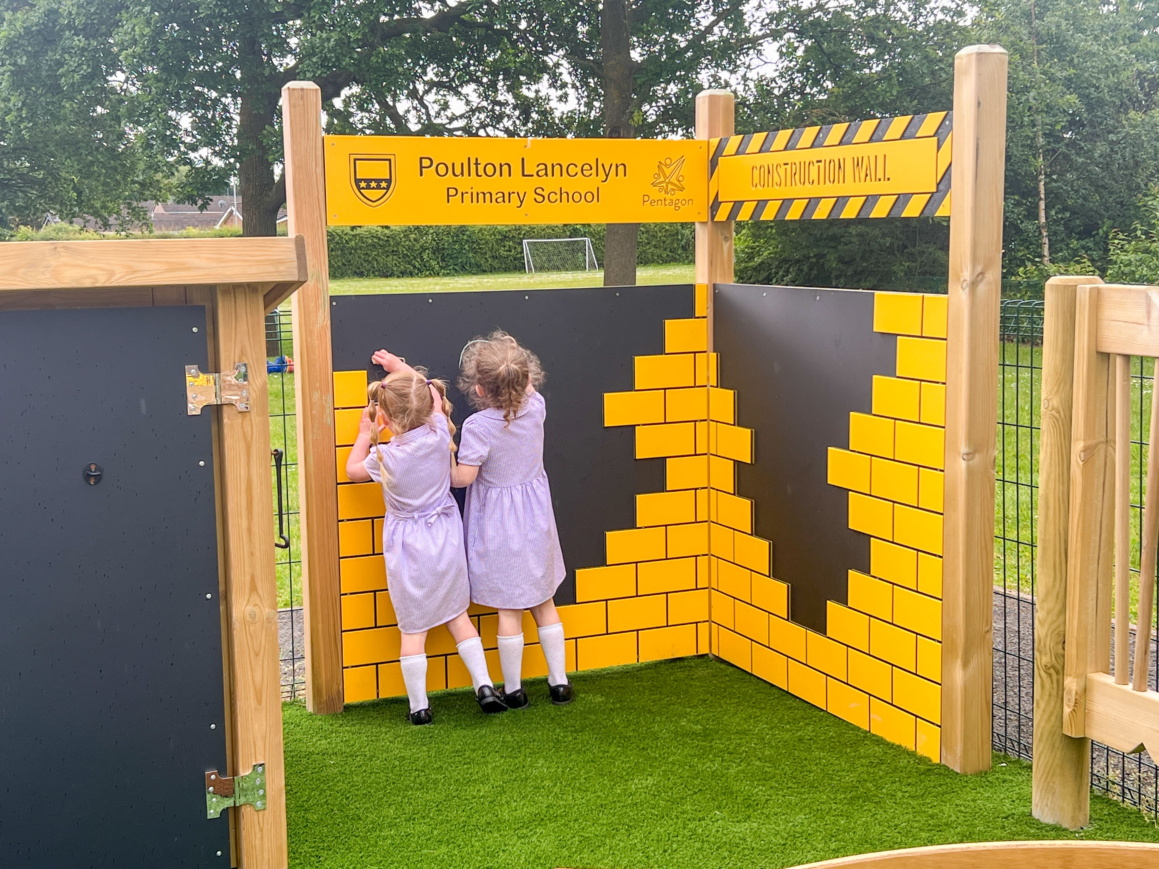 Two little girls are writing on a chalkboard that has been bespokely designed to showcase the school's badge and name.
