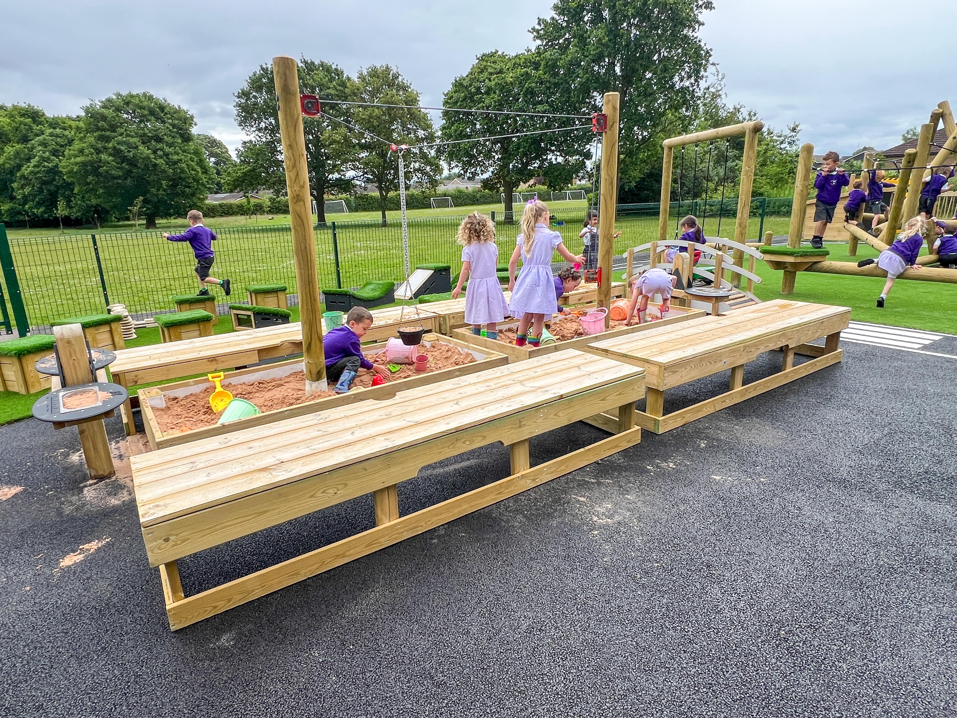 A group of children are playing in the large sandbox, creating structures out of the sand/