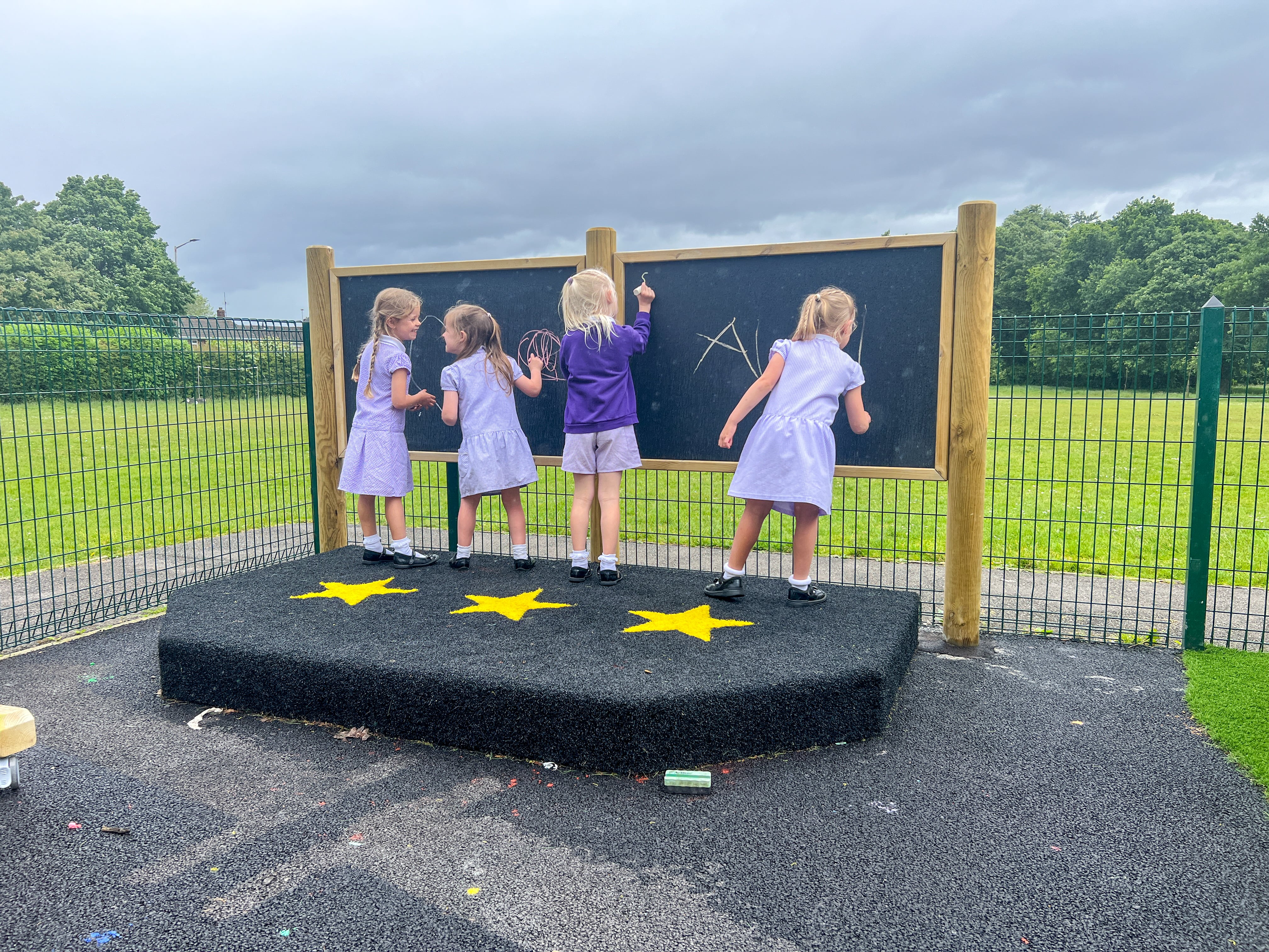 Four girls are stood on the performance stage and are writing on the chalkboard that it attached to it.