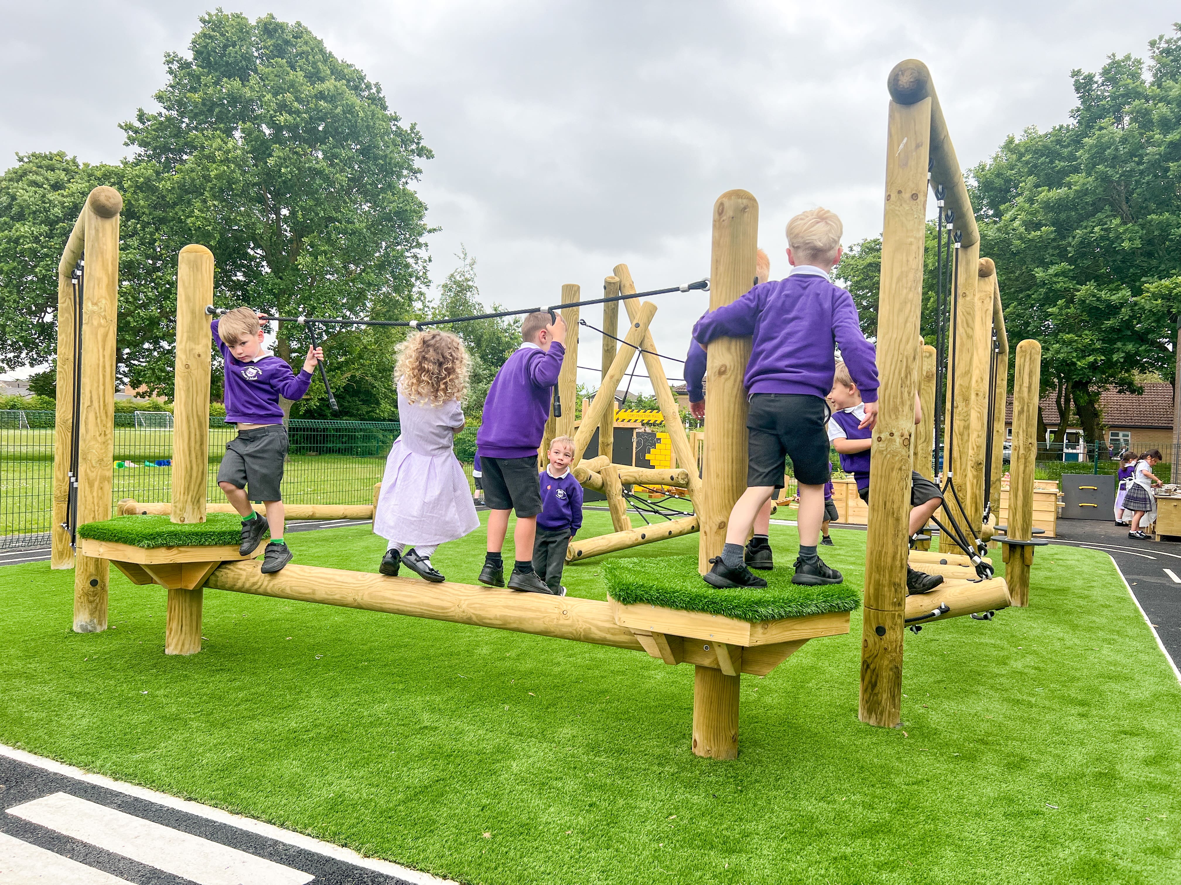 A group of children are playing on active play equipment, tackling a trim trail.