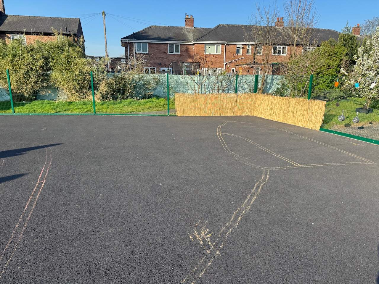An empty playground with faded thermoplastic markings and a wooden fence in the corner.