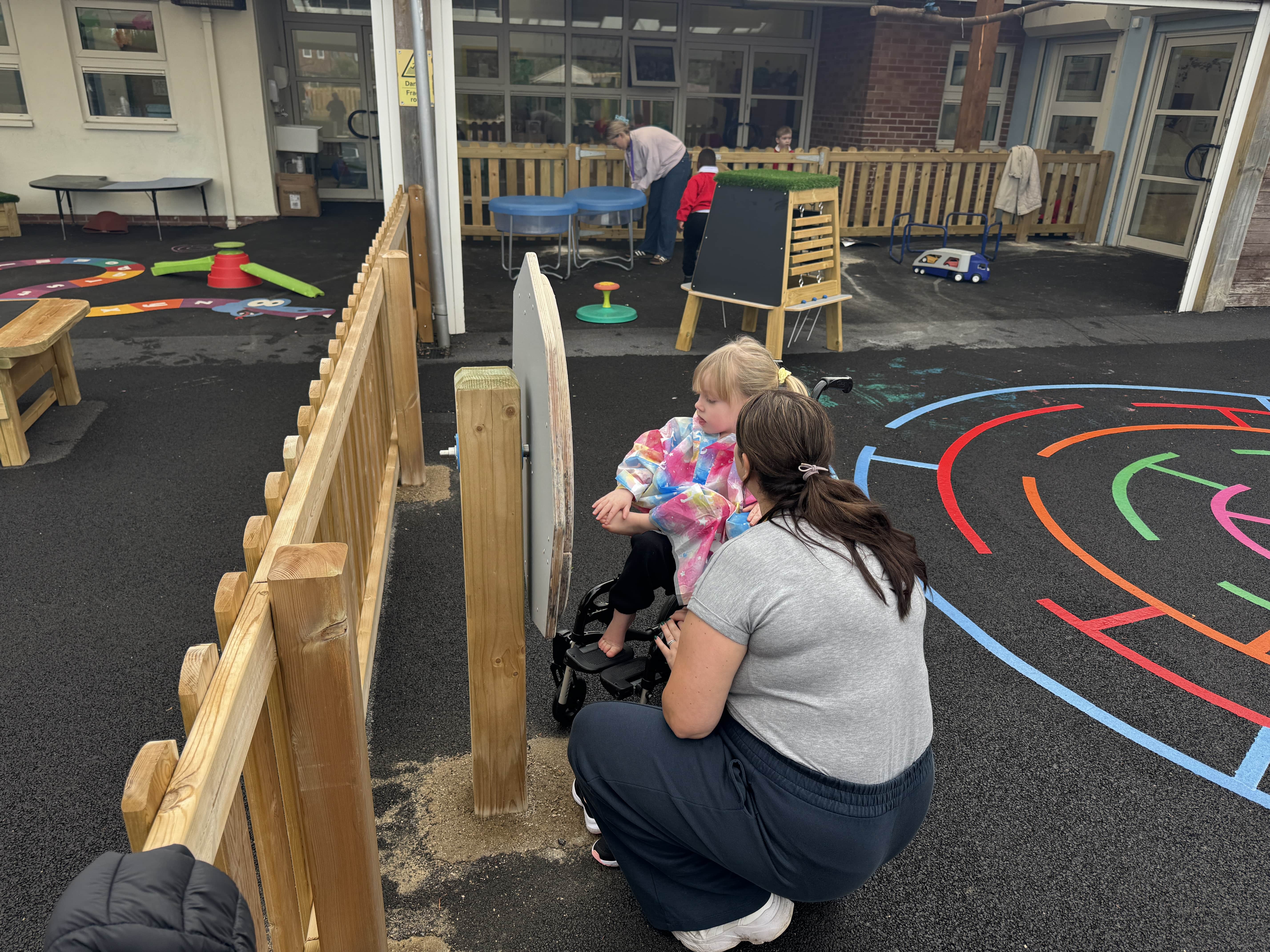 A little girl is playing with a sensory spinner as a teacher is helping the child.
