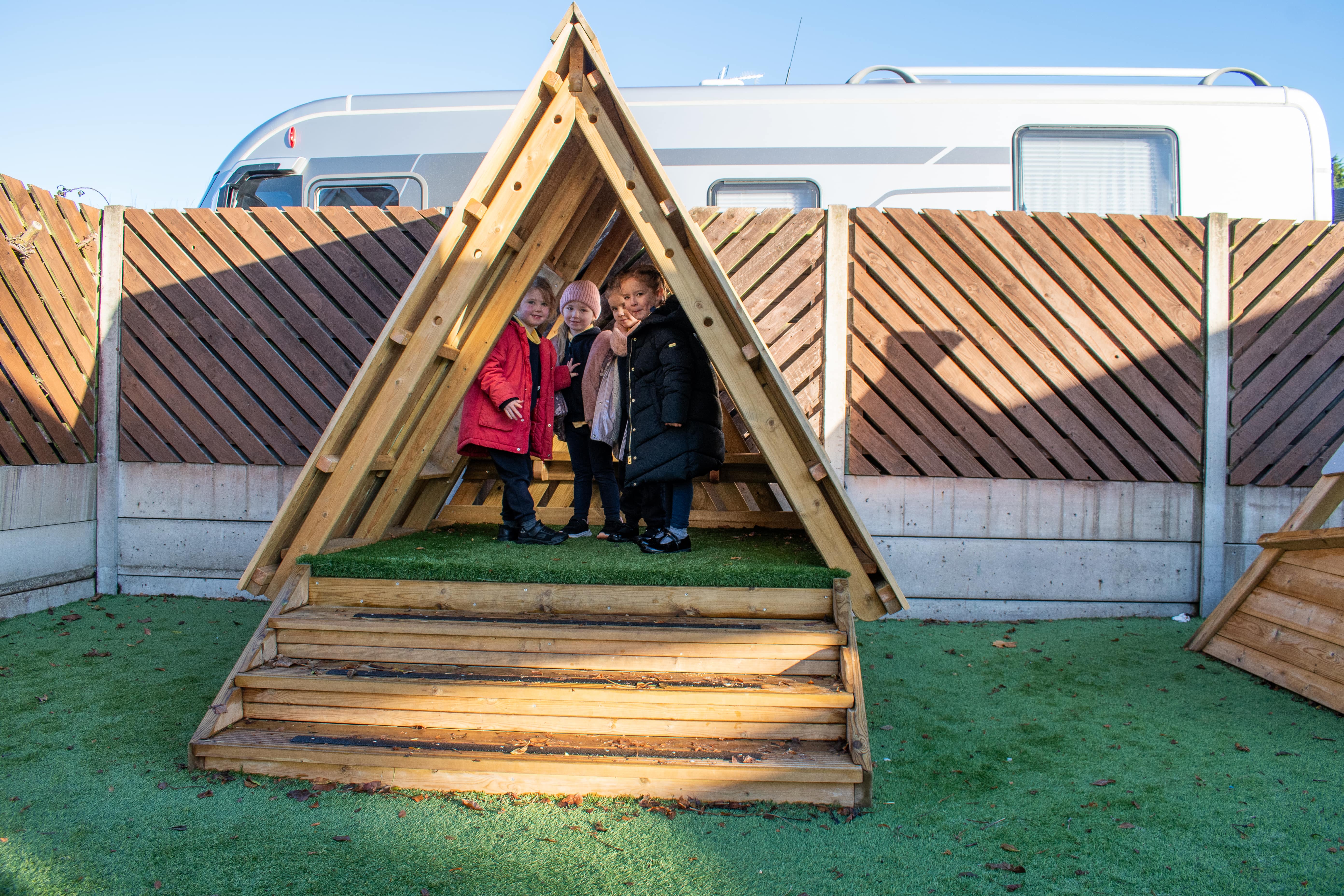 Three kids are sat underneath a learning den as they smile at the camera.