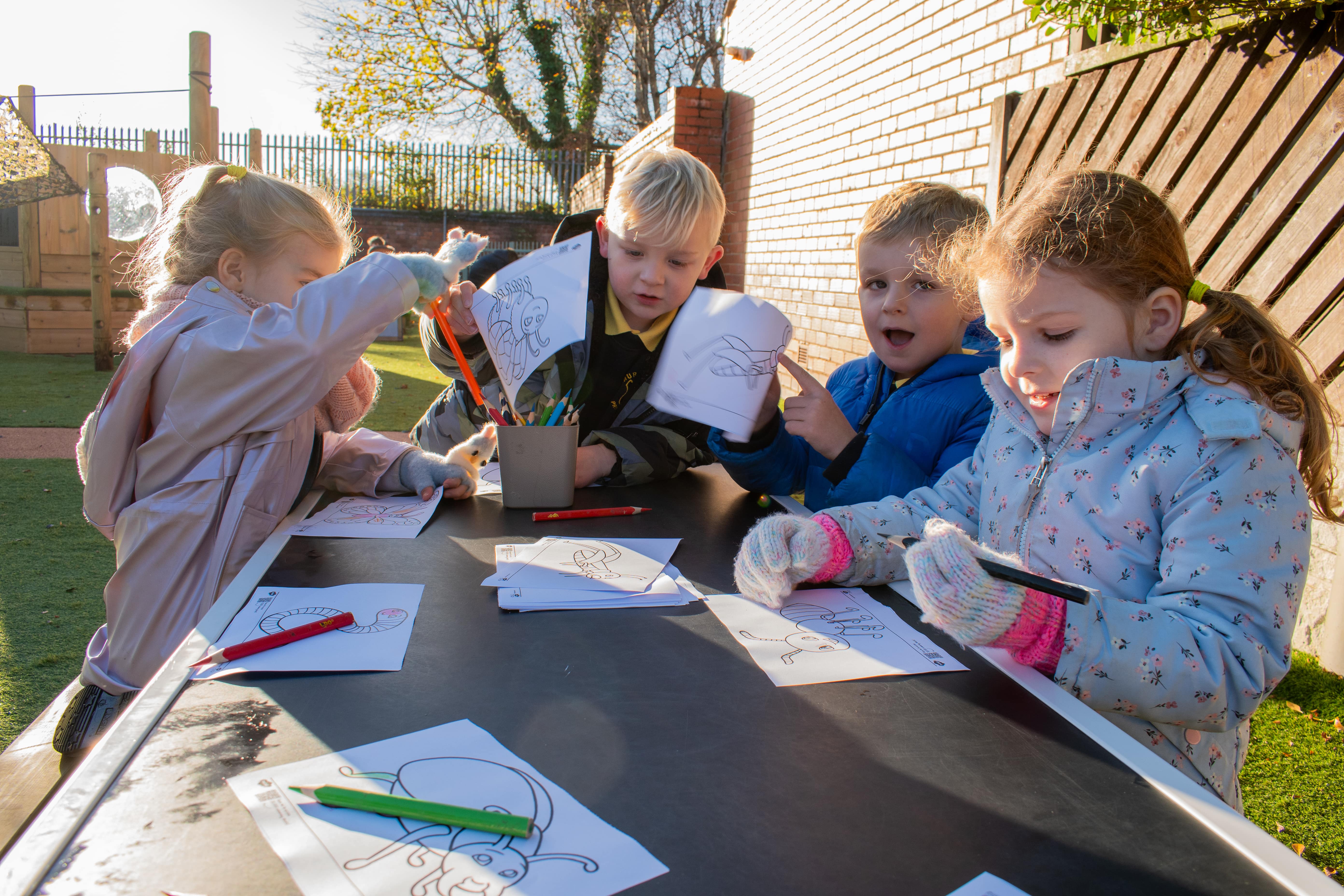 A group of four children are colouring in sheets as they play together.