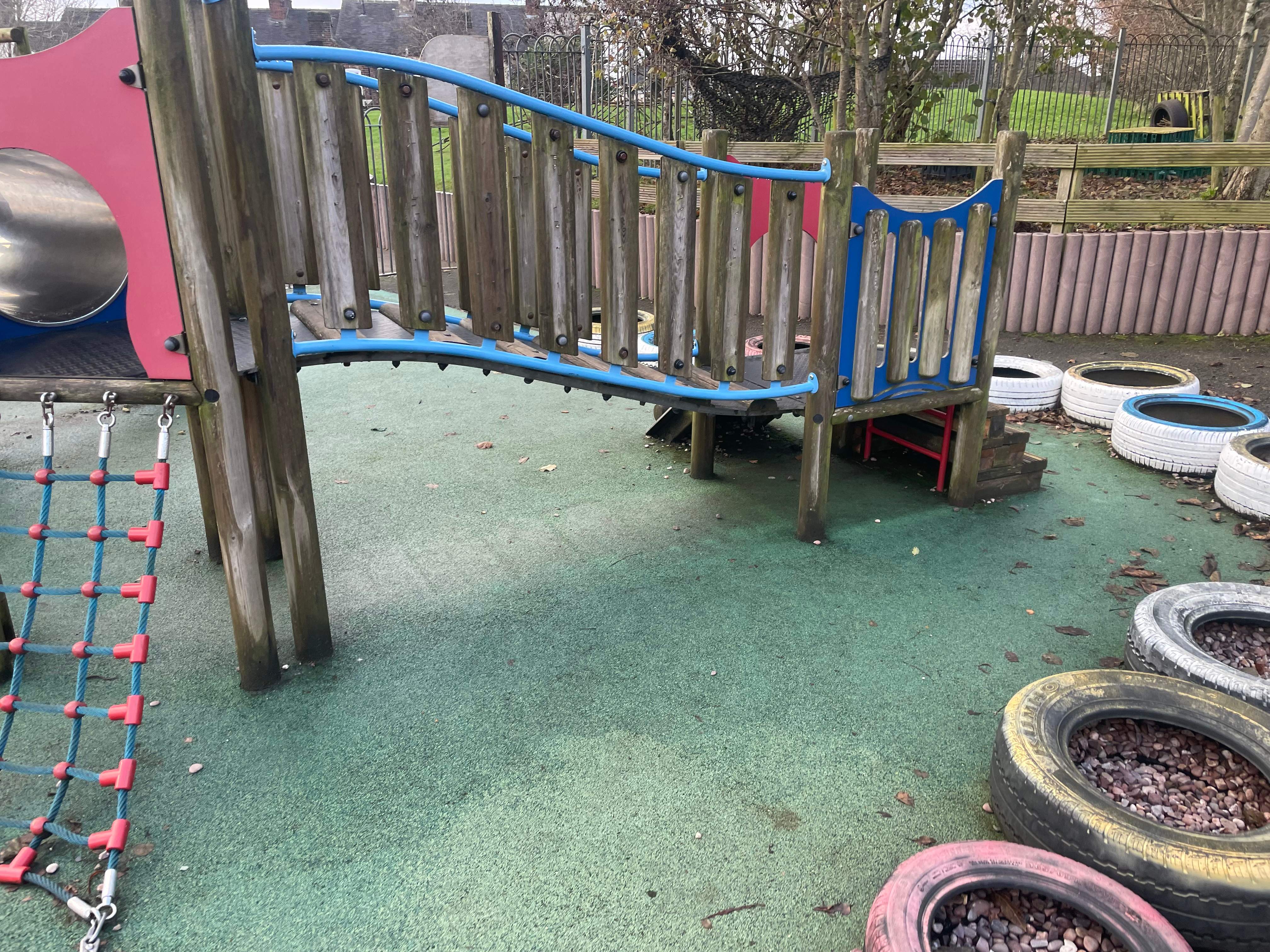 An old playground tower, with worn down wood and worn-out green wetpour surfacing.