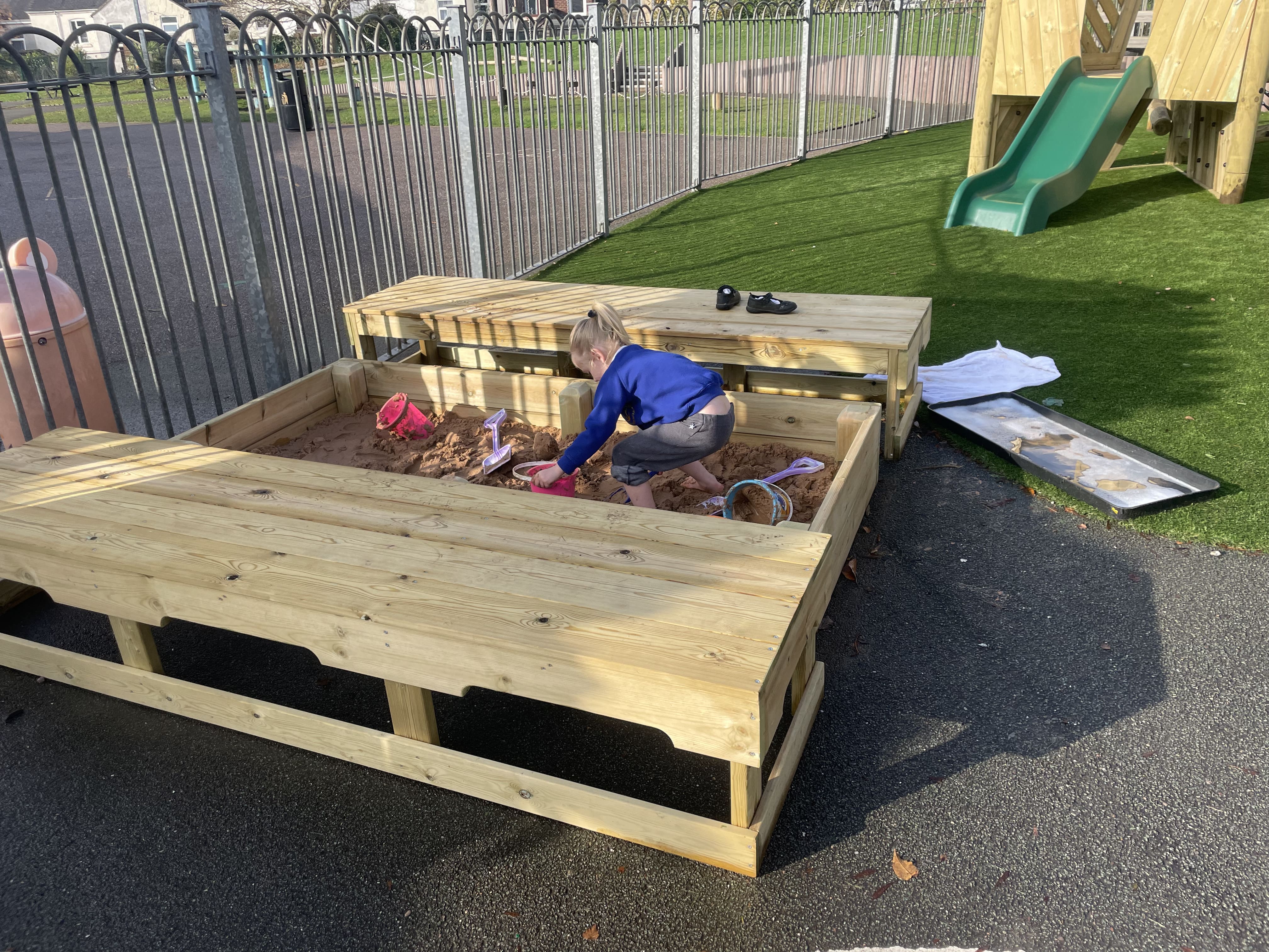 A little child is playing in a large sandbox, as they dig through sand and use a variety of pieces of equipment.