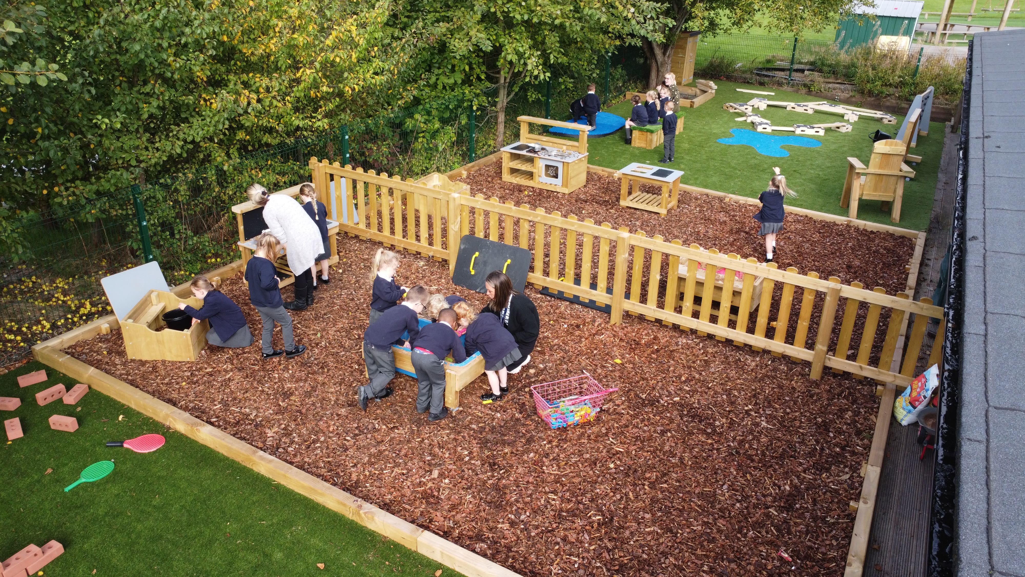 A large group of reception children are playing in the mud kitchen area and are creating a variety of new and unique dishes.
