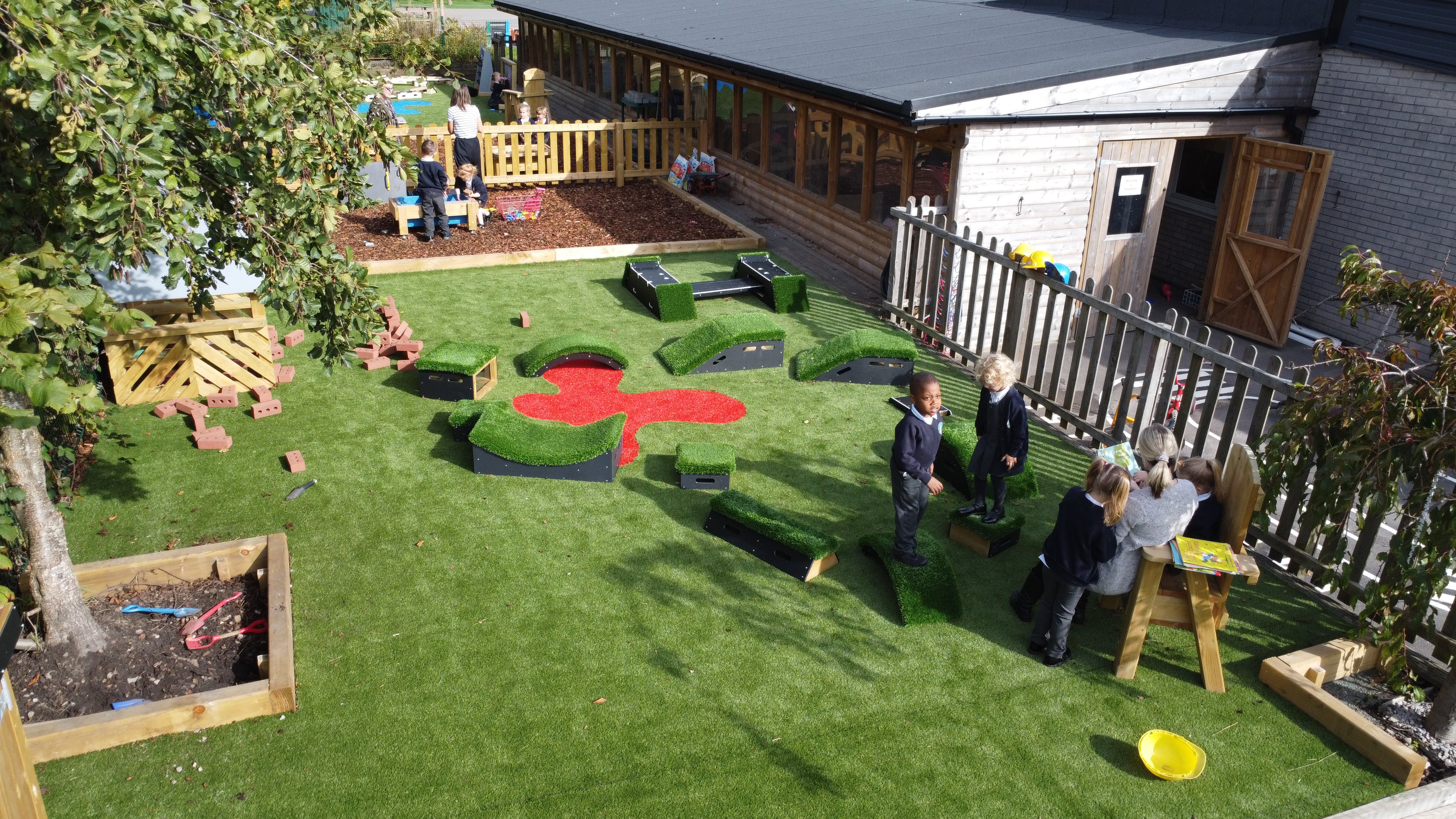 The reception playground with the new artificial grass surfacing and freestanding play equipment, with a mud kitchen area being seen.