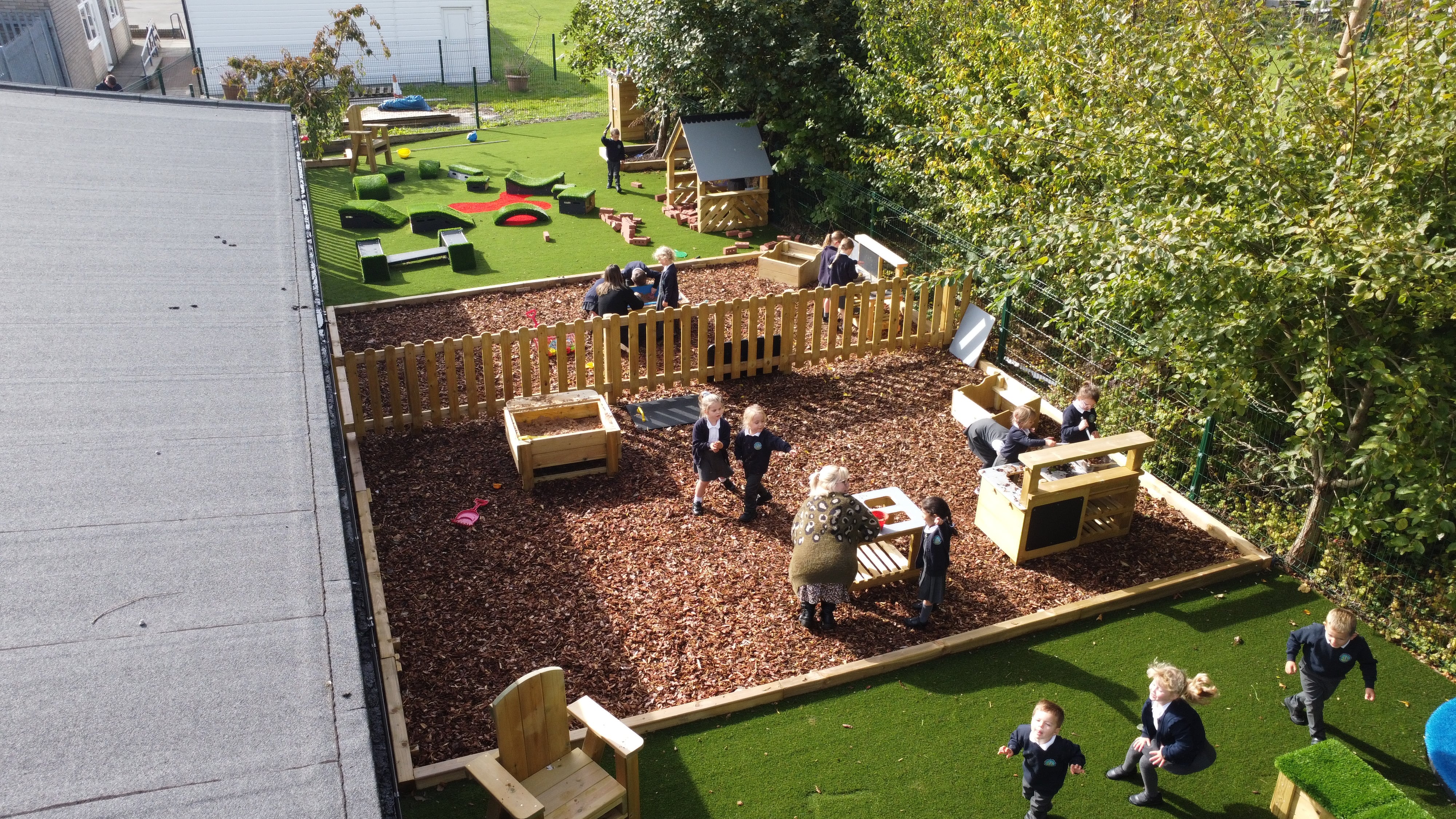 A Rubber Bark area with mud kitchens placed on top of it, with children playing with them.