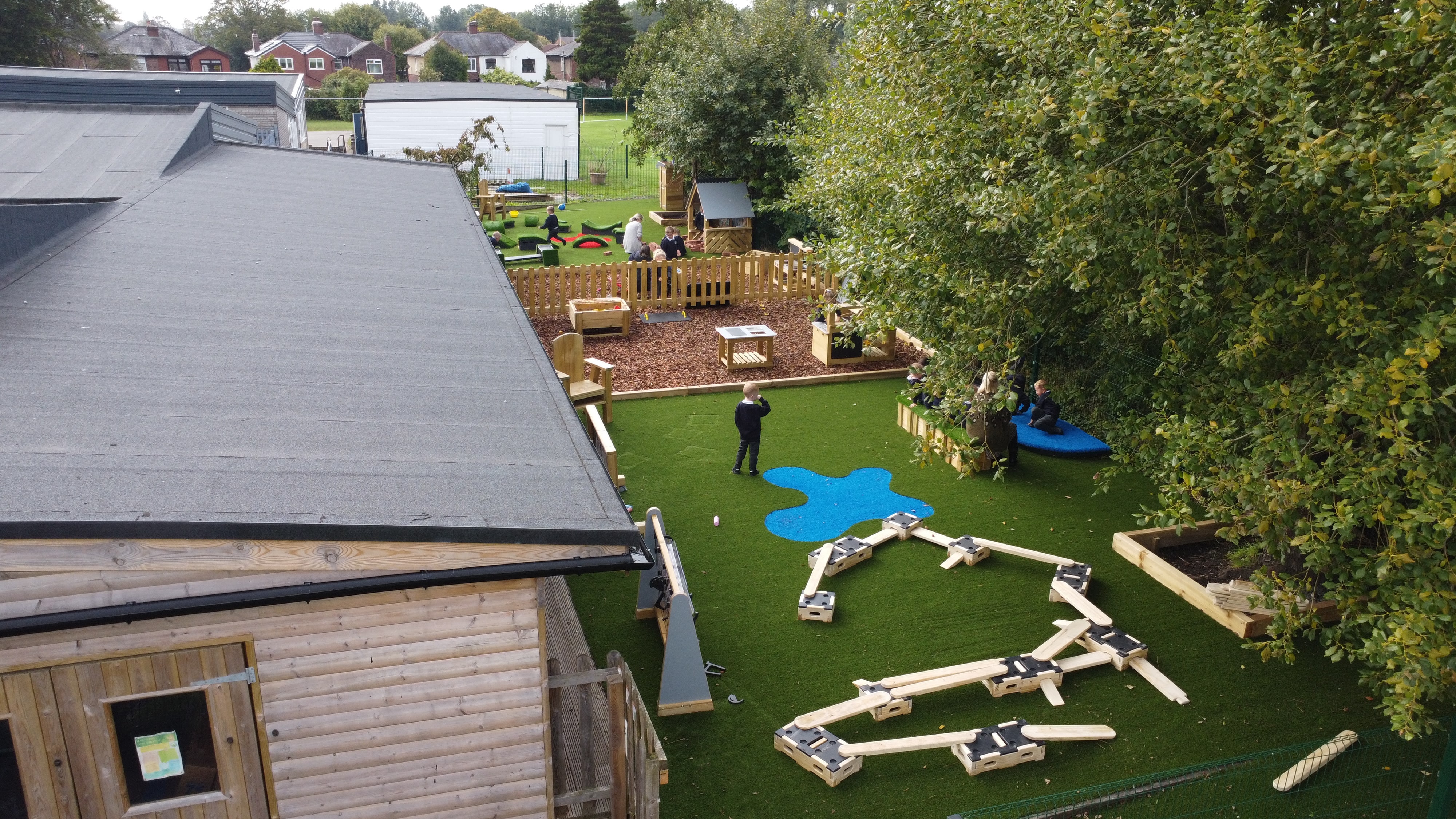 An artficial grass nursery playground, with play builder pieces and a mud kitchen area.