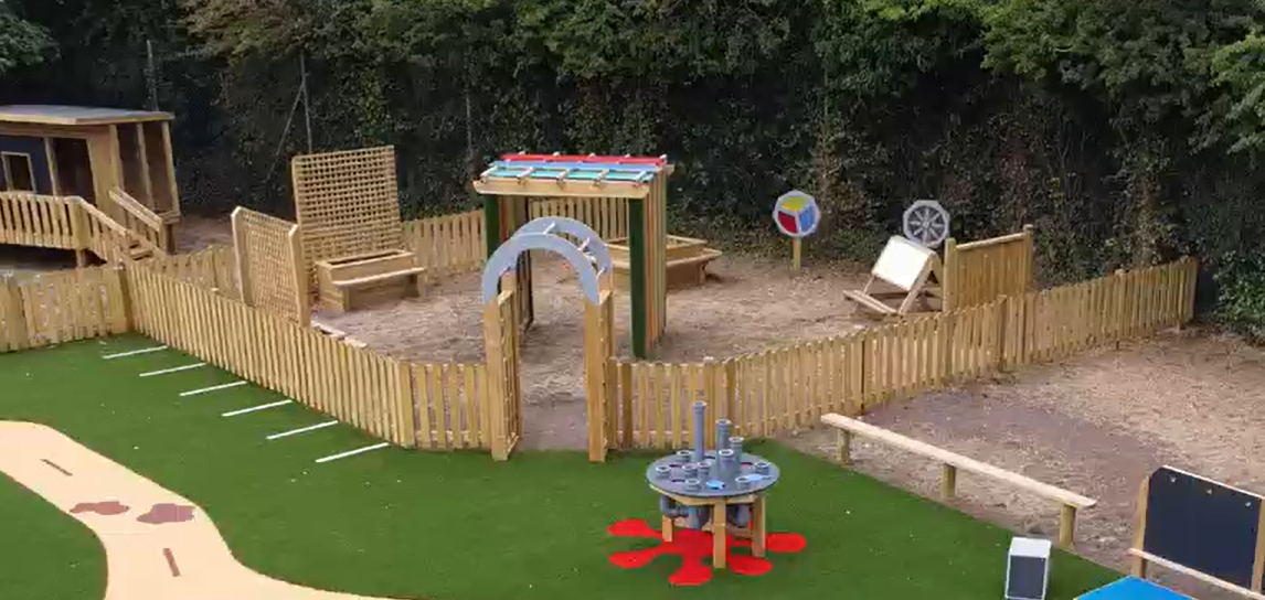 A sensory garden that contains a variety of different pieces of play equipment, which is zoned off by bowtop fencing.