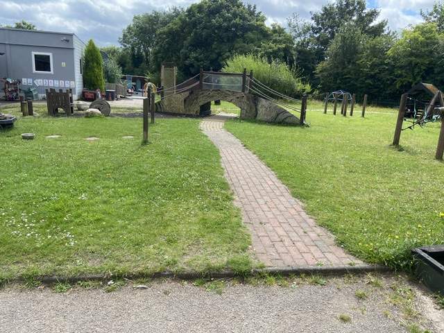 An old playground with natural grass and a worn out cobbled path in the middle, with a piece of old play equipment.