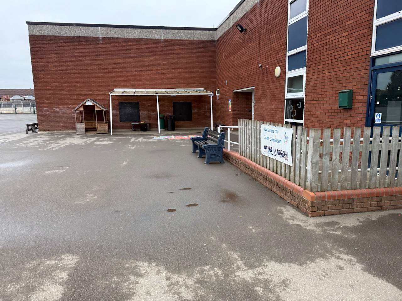An old tarmac playground with muddy puddles and old fencing.