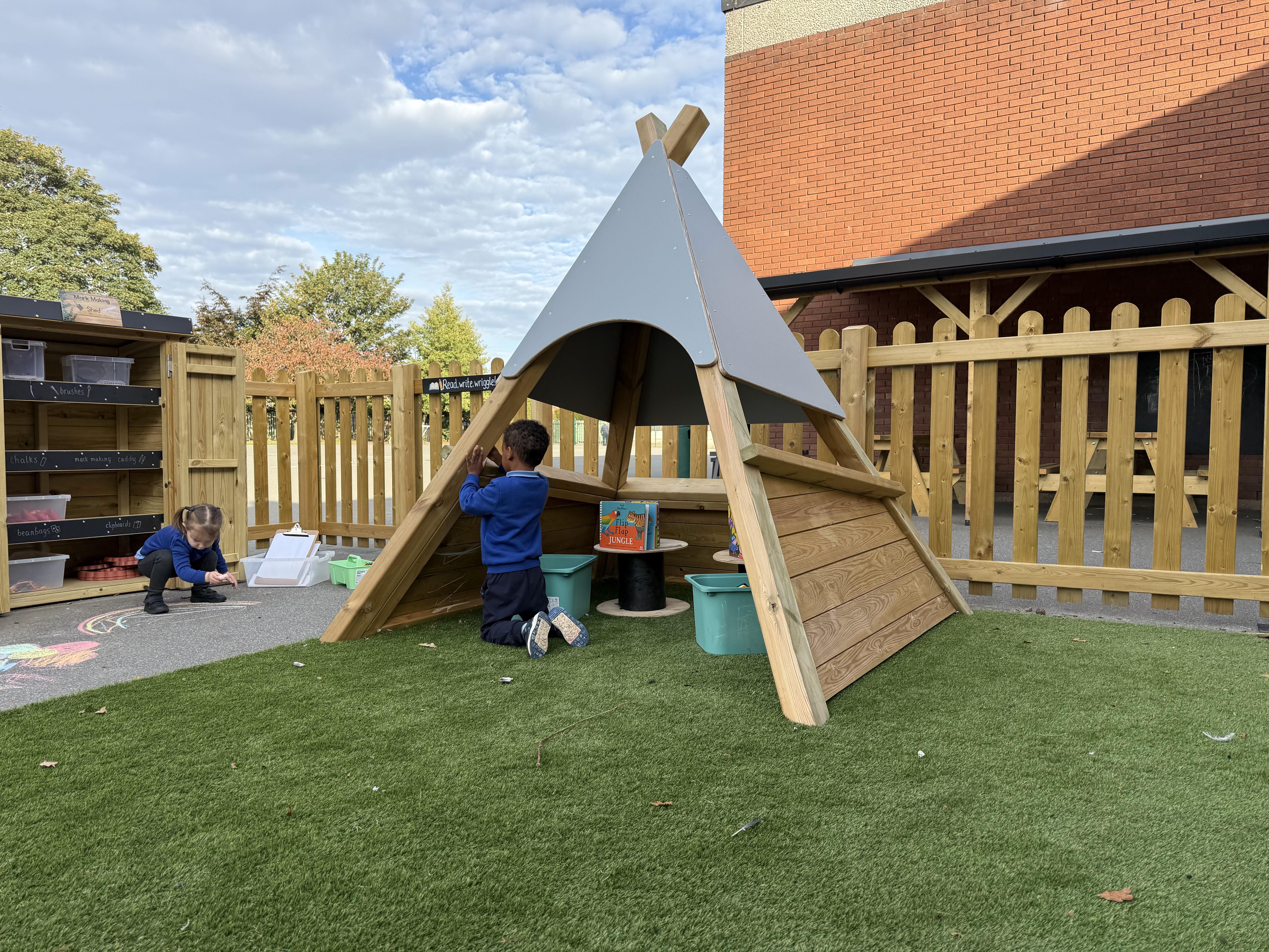 A little boy is peering outside of the Wigwam, watching another child retrieve items from the Acorn Self-select store.